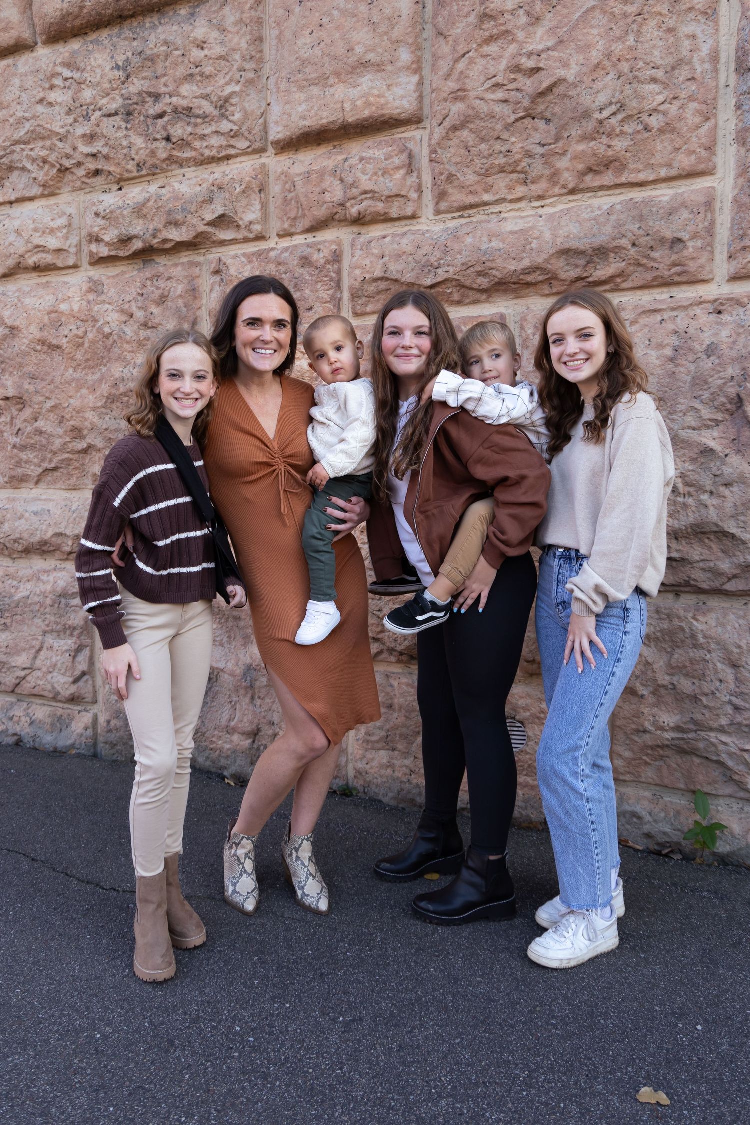 Group photo against stone wall with people wearing coordinated brown and neutral tones.