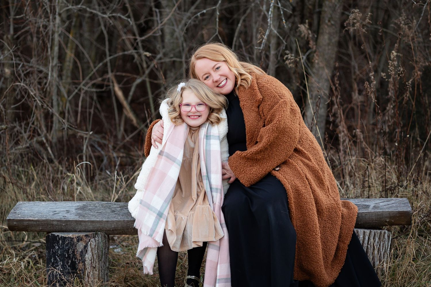Two people share a tender moment while sitting on a wooden bench outdoors.