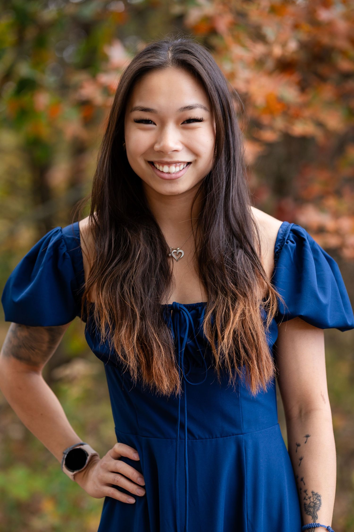 Woman in navy blue dress with puff sleeves smiles warmly against autumn foliage.