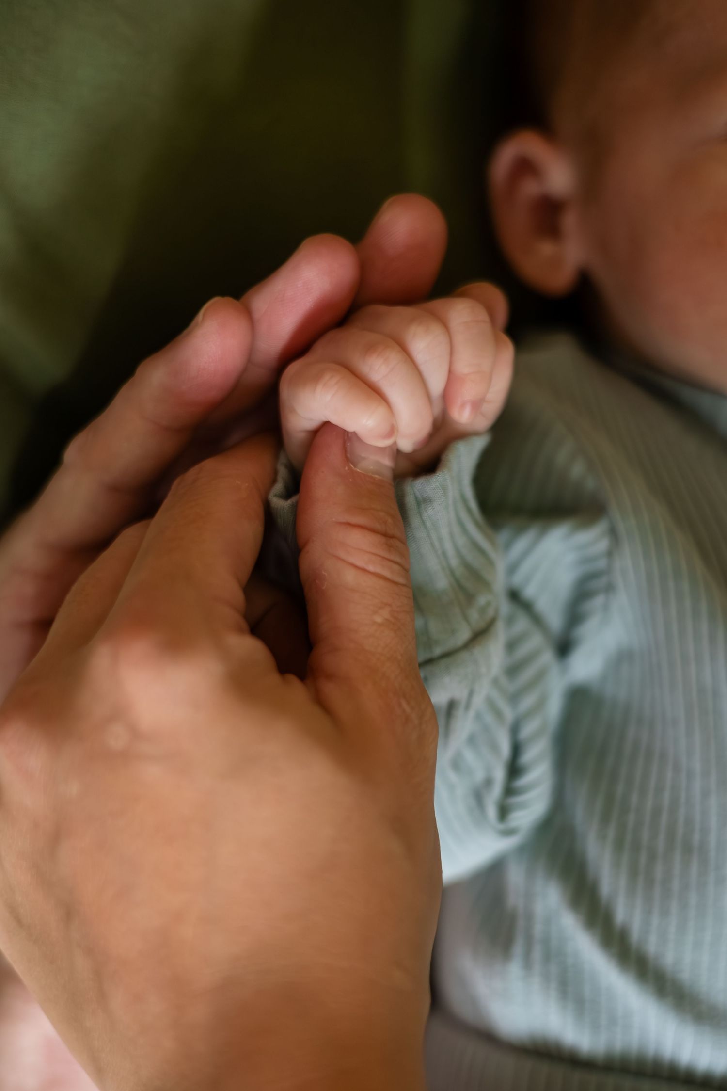Close-up detail of tiny infant fingers against mint green fabric.