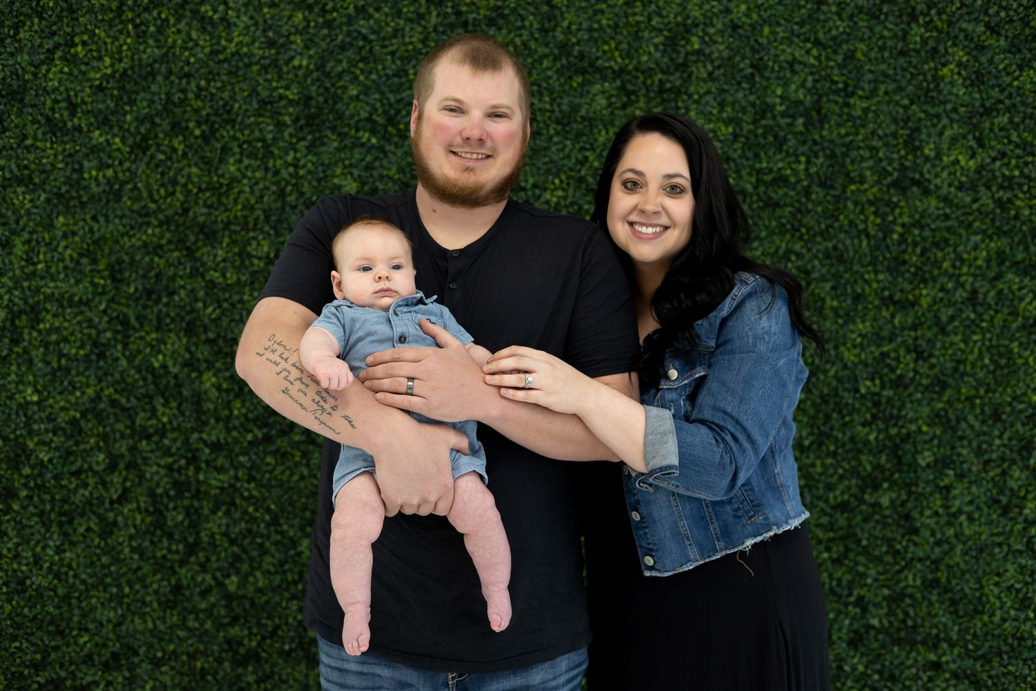 A family portrait against a green hedge background showing casual denim and relaxed style.