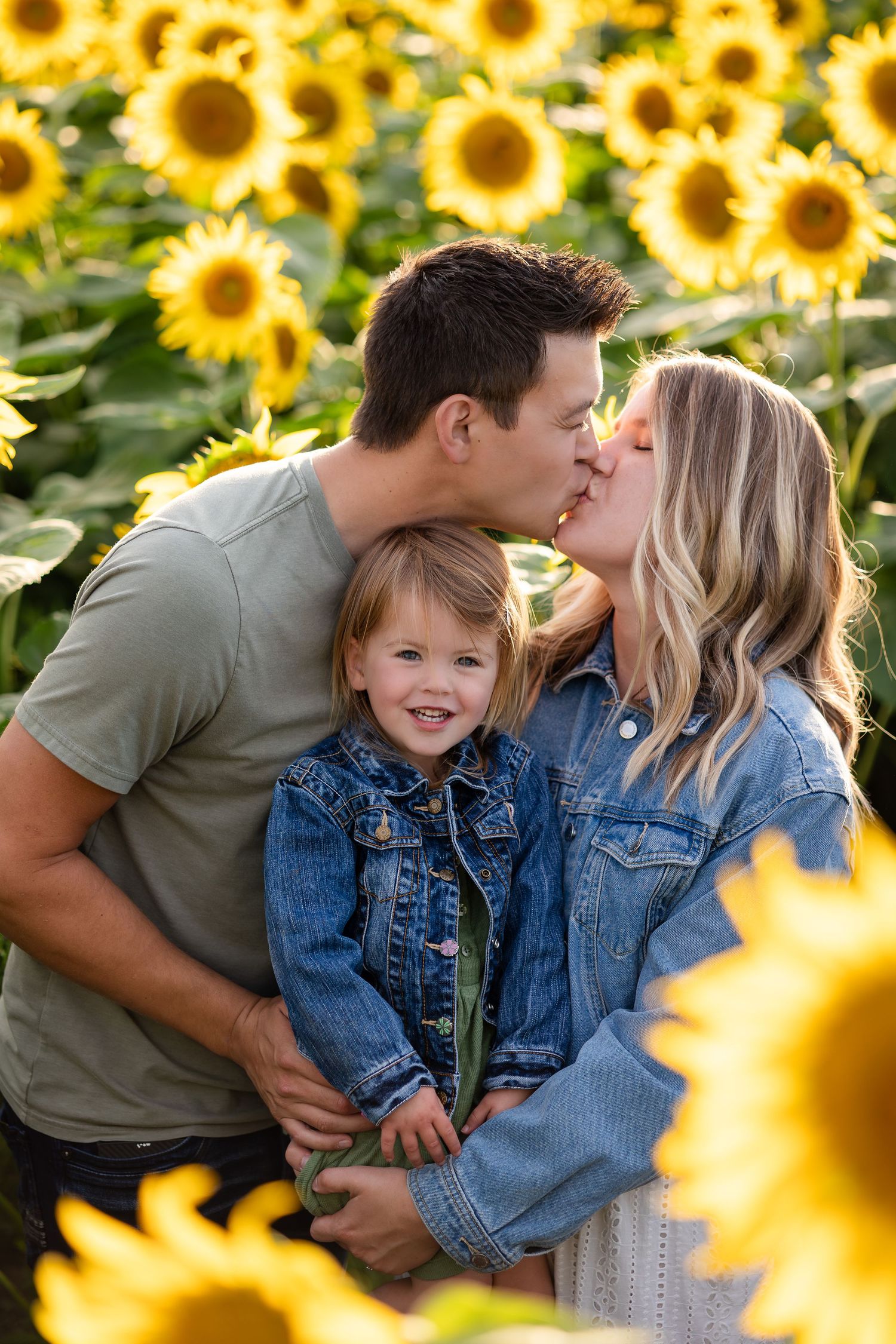 Candid family moment captured in a sunflower field during sunset.