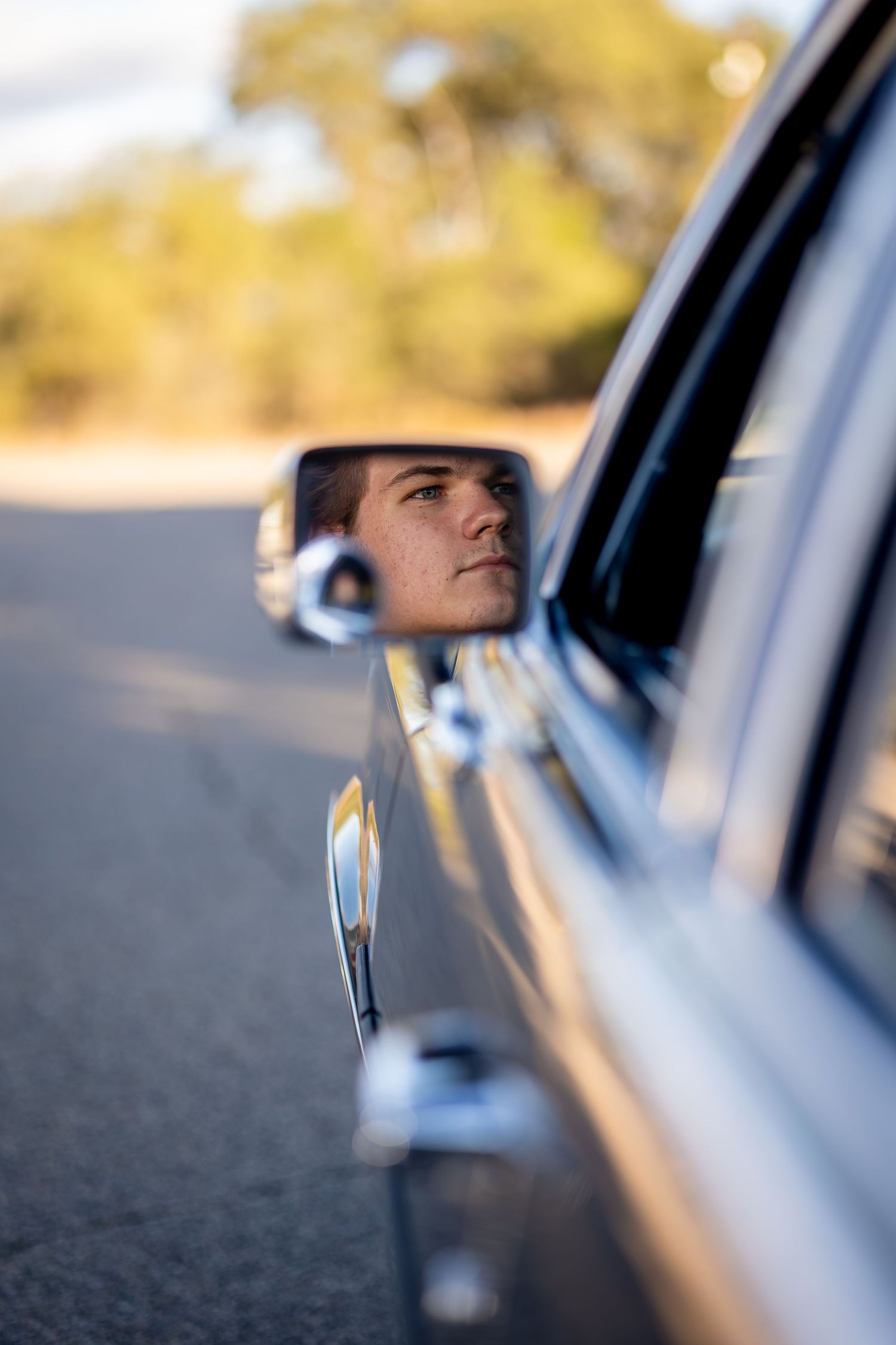 Car side mirror reflection shows blurred background and driver's perspective on sunny day.