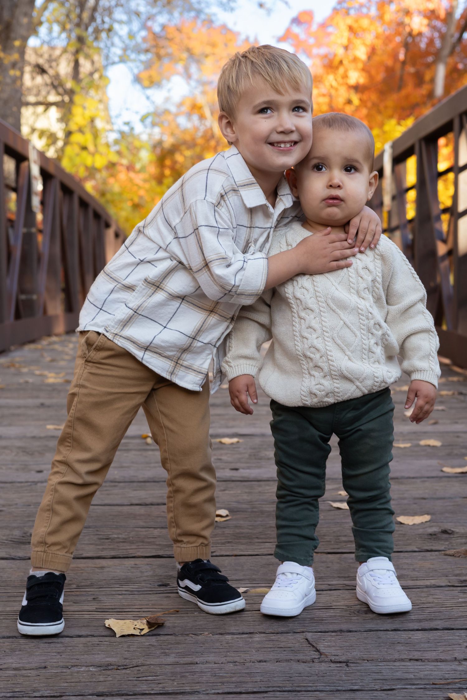 Two small children in casual wear playing together on a wooden bridge in fall.