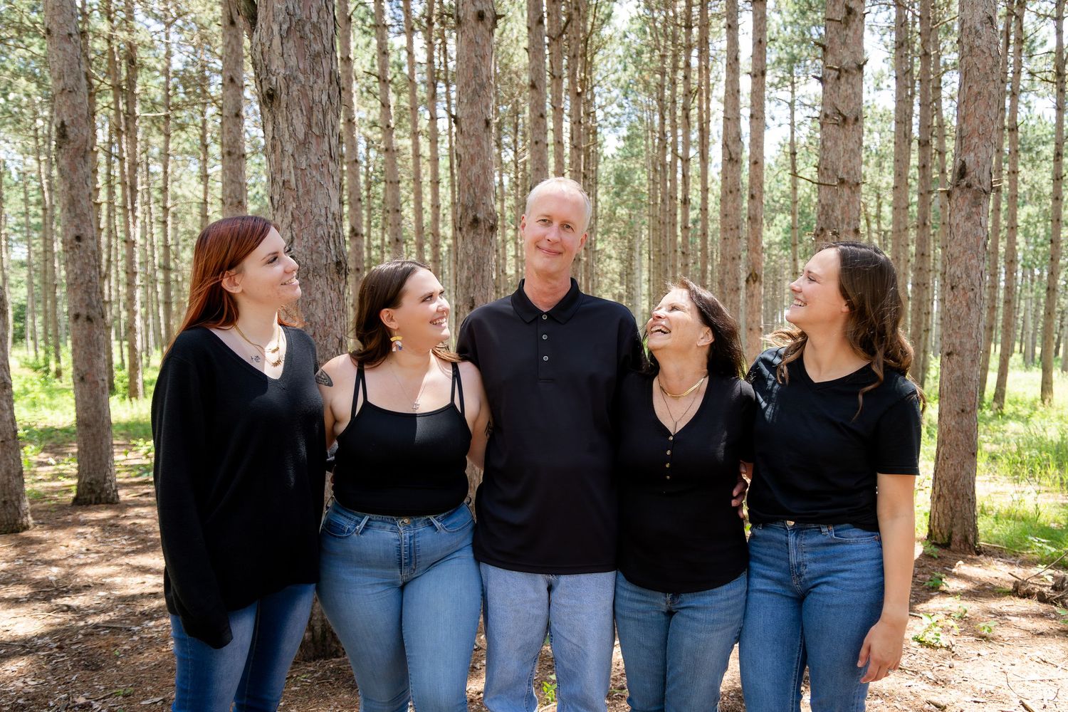 Group wearing coordinated black tops and jeans posing together in a pine forest.