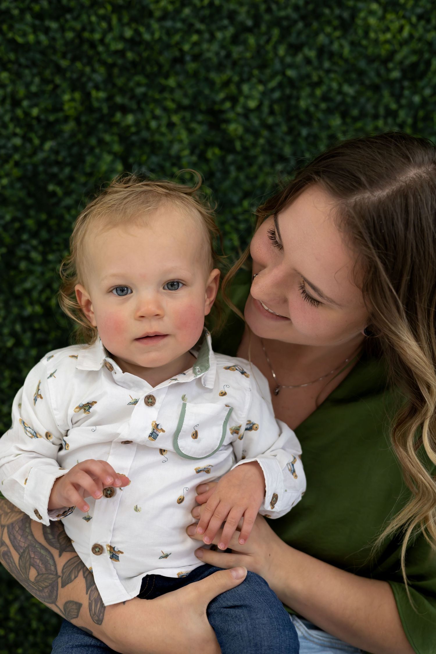 A heartwarming parent-child portrait against a lush green hedge backdrop.