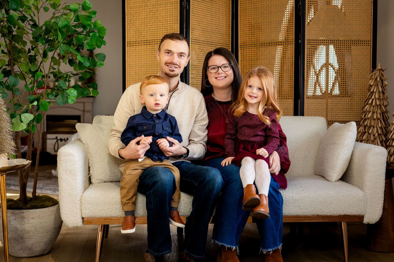 Happy family of four posing together on a white couch in a cozy, modern living room setting.