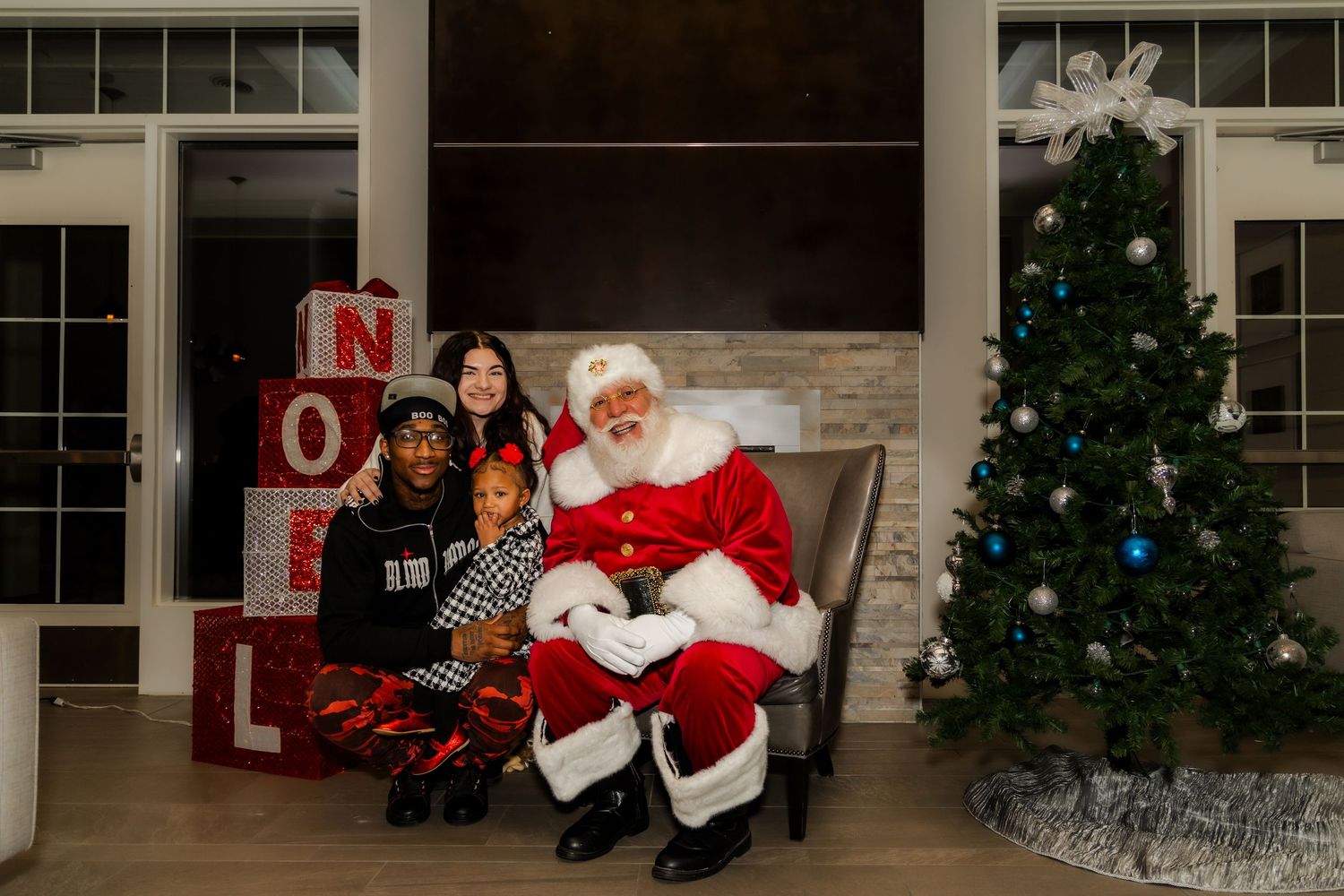Christmas photography setup with decorated tree and NOEL letters against stone wall.