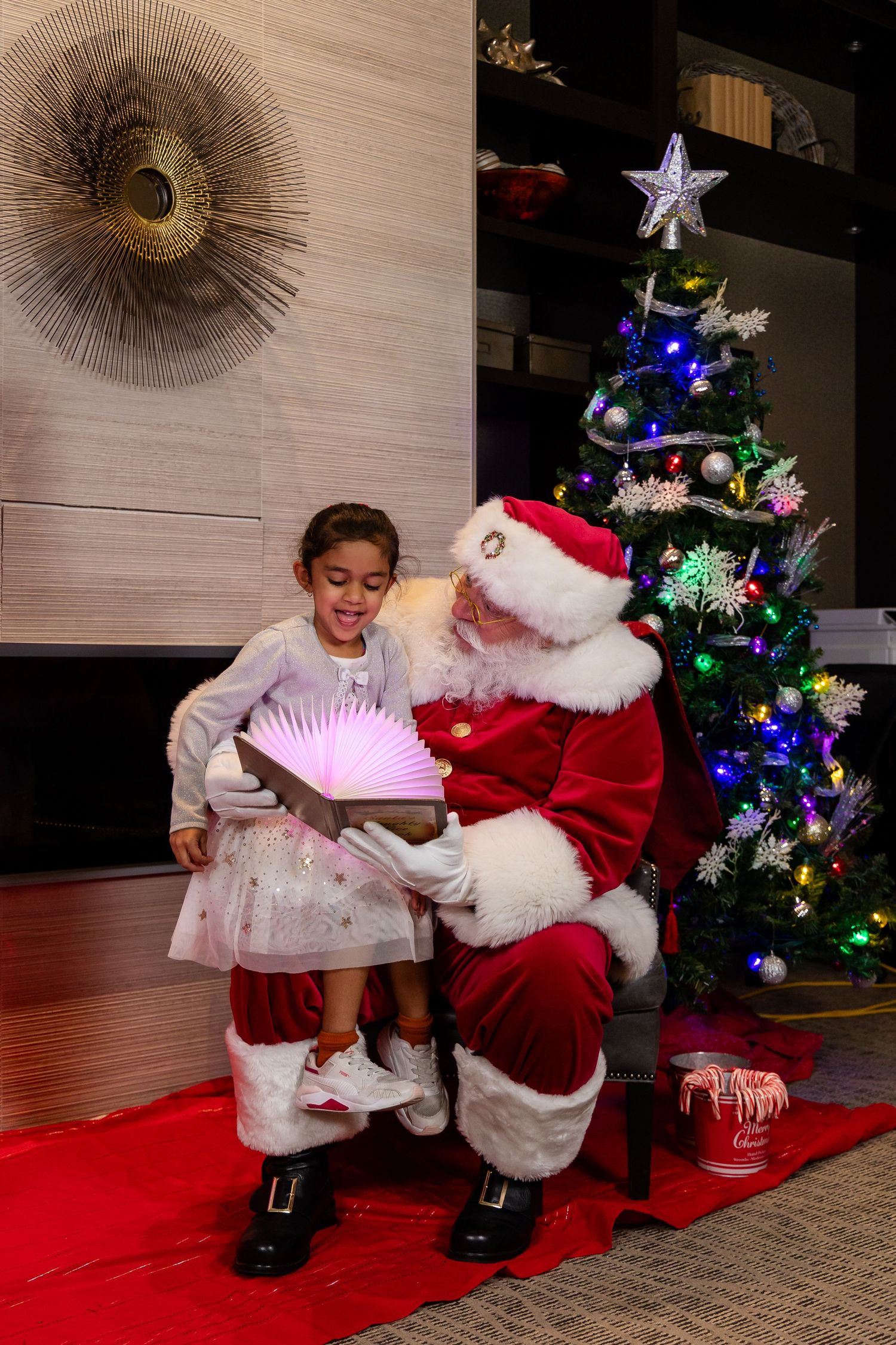A joyful holiday moment captured near a Christmas tree with Santa in his classic red and white suit.