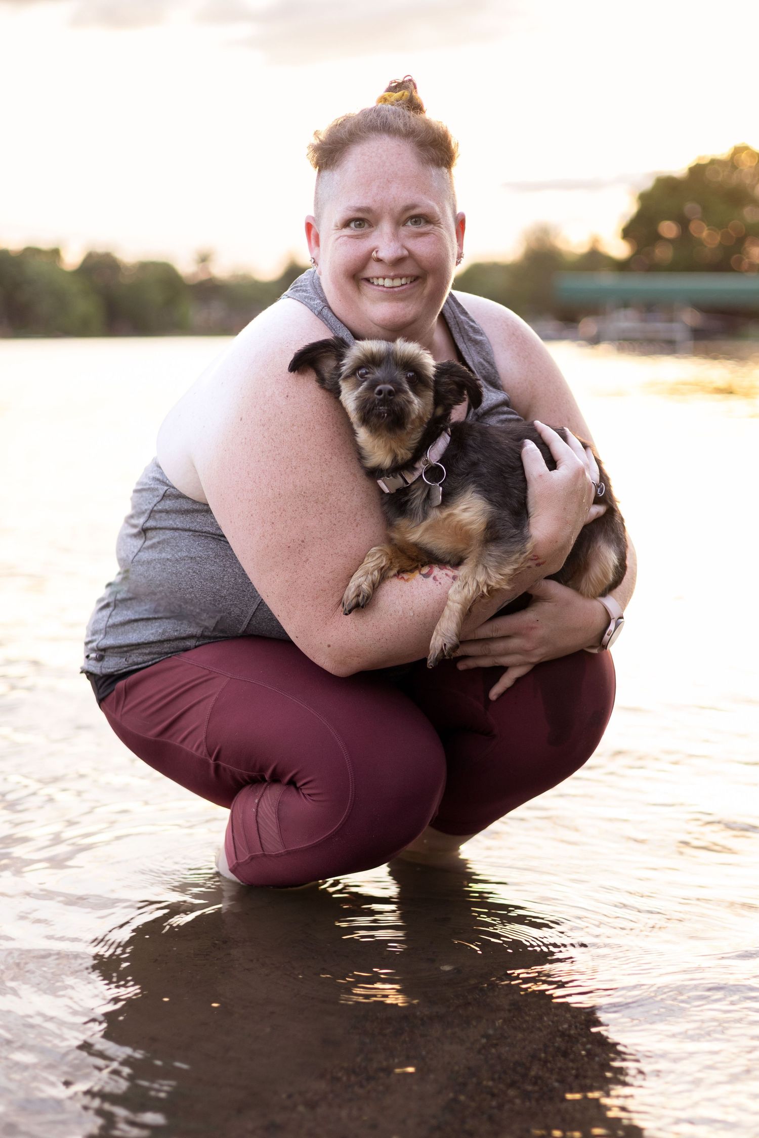 A small dark dog being held at the beach during sunset.