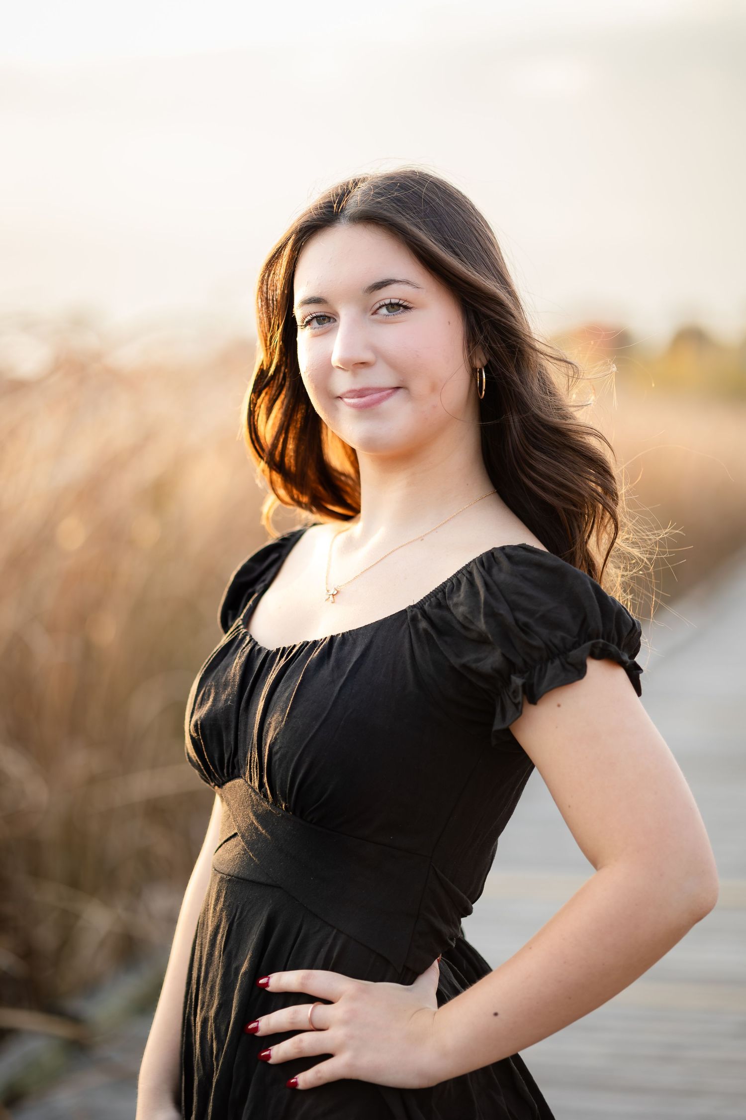 Outdoor portrait in black dress with ruffled sleeves on wooden walkway.