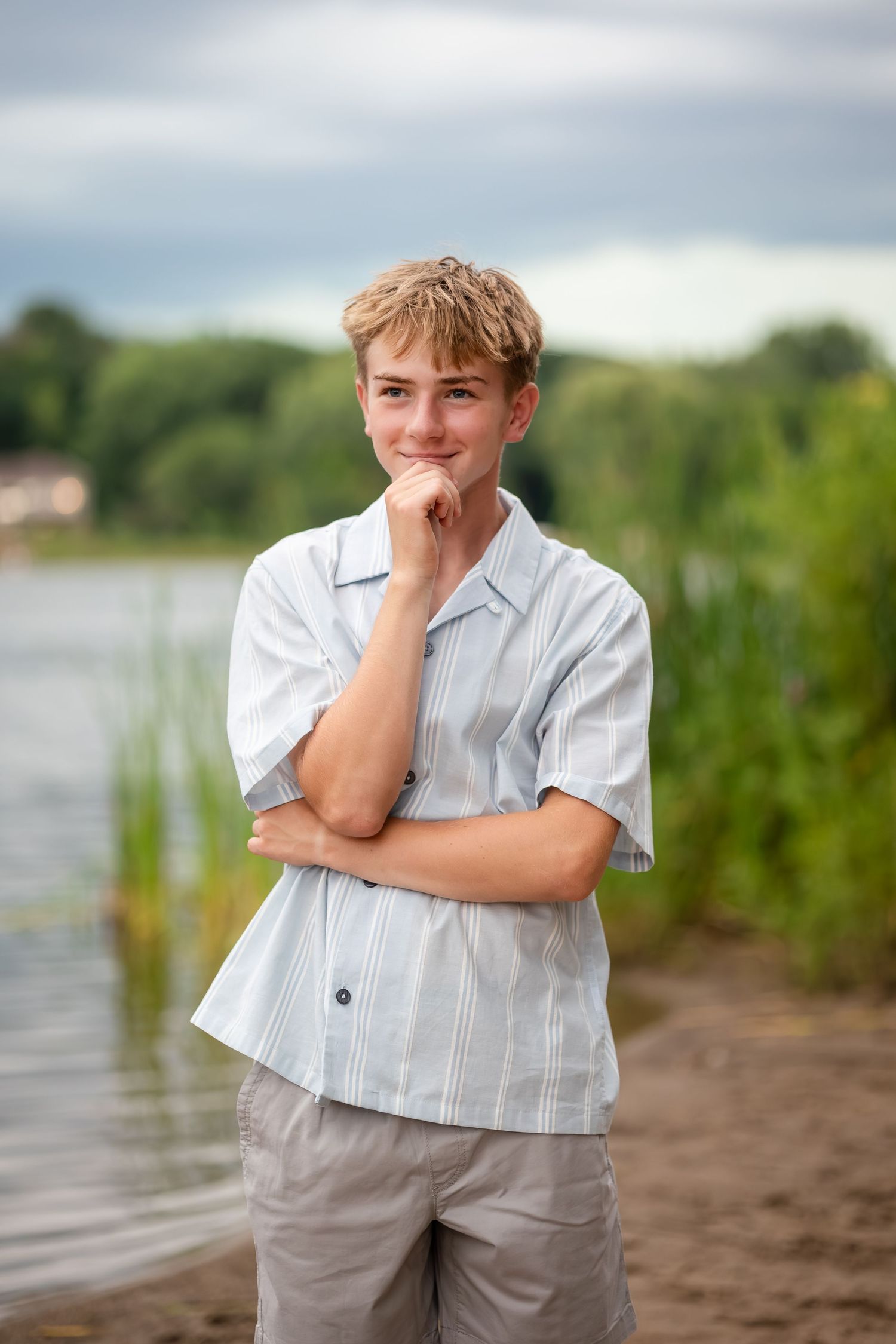 Person in white button-down shirt poses thoughtfully by waterfront with natural scenery.