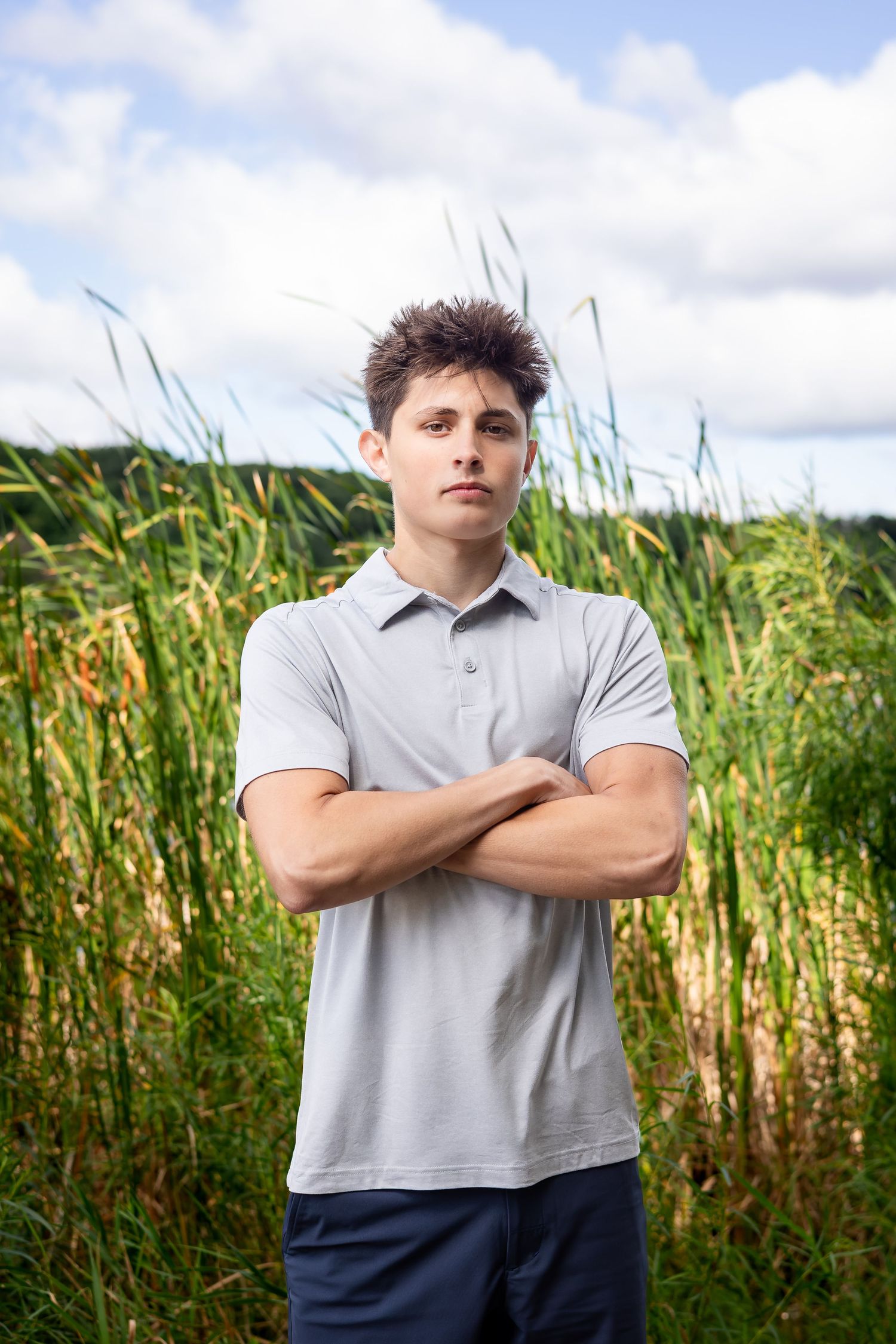 Person in gray polo shirt poses confidently against tall grass field background.