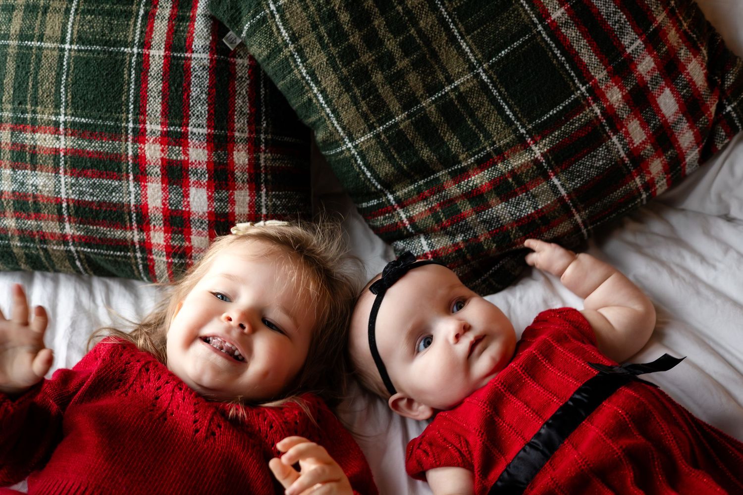 Children snuggled under a cozy plaid blanket with Christmas decorations in the background.