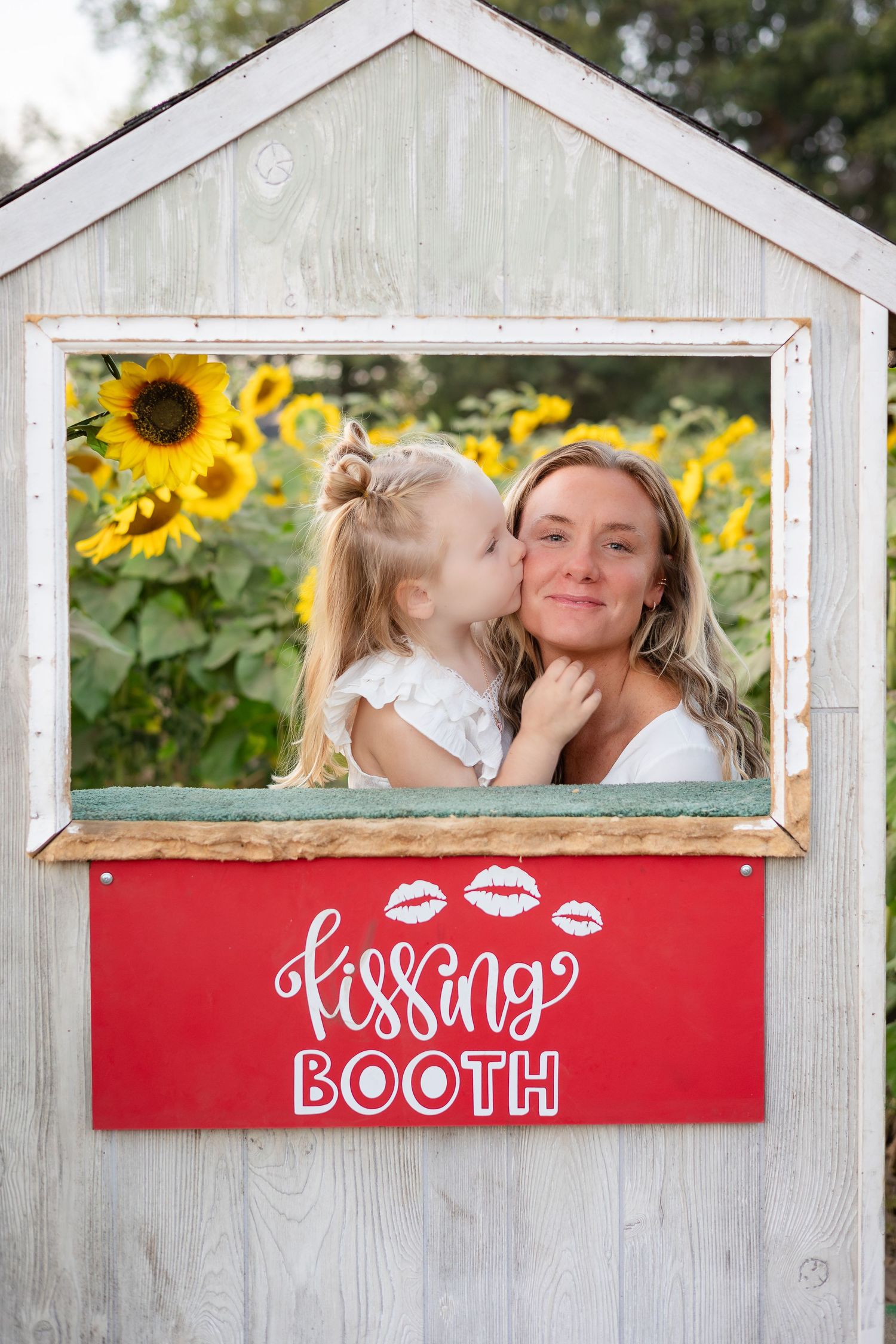 Red and white kissing booth frame with sunflowers visible in background.