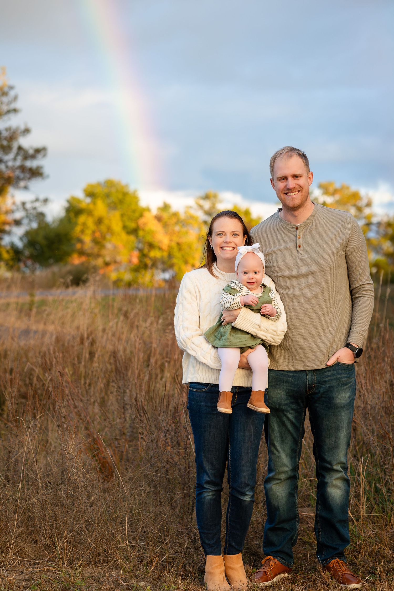 A family portrait in a field with a rainbow visible in the background during golden hour.