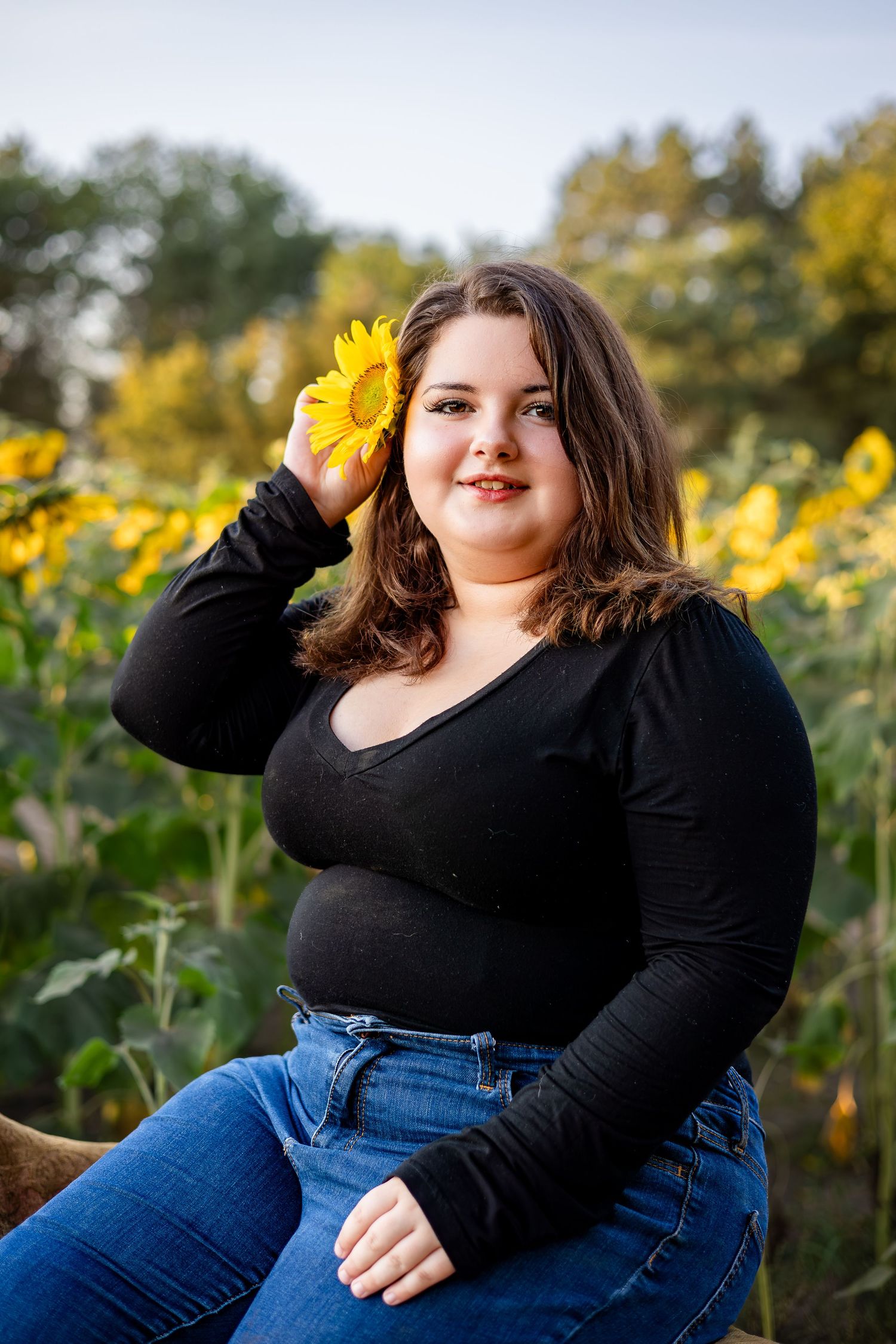 Portrait session in a sunflower field featuring casual black top and blue jeans against bright yellow blooms.