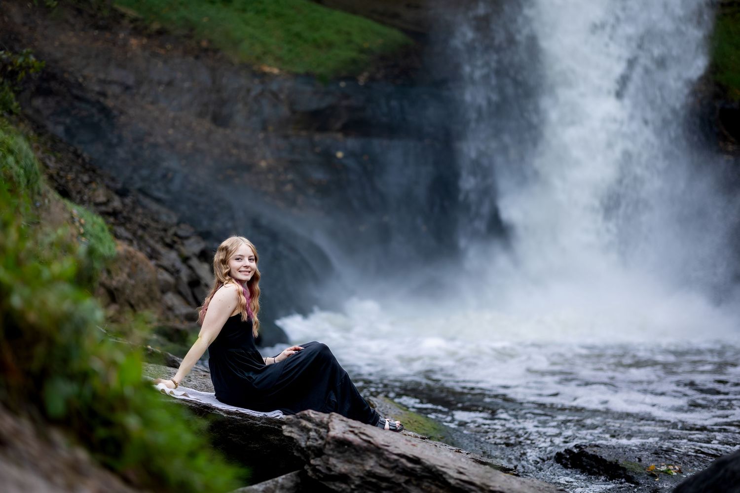A person explores a scenic waterfall cascade surrounded by lush greenery and rocky terrain.