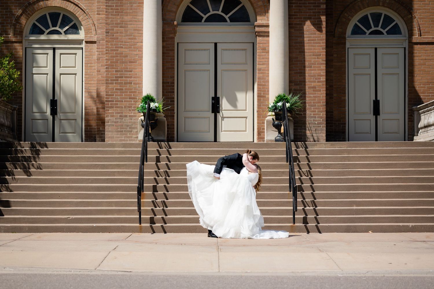 Bride and groom share a romantic dip pose on church steps in elegant wedding attire outdoors.