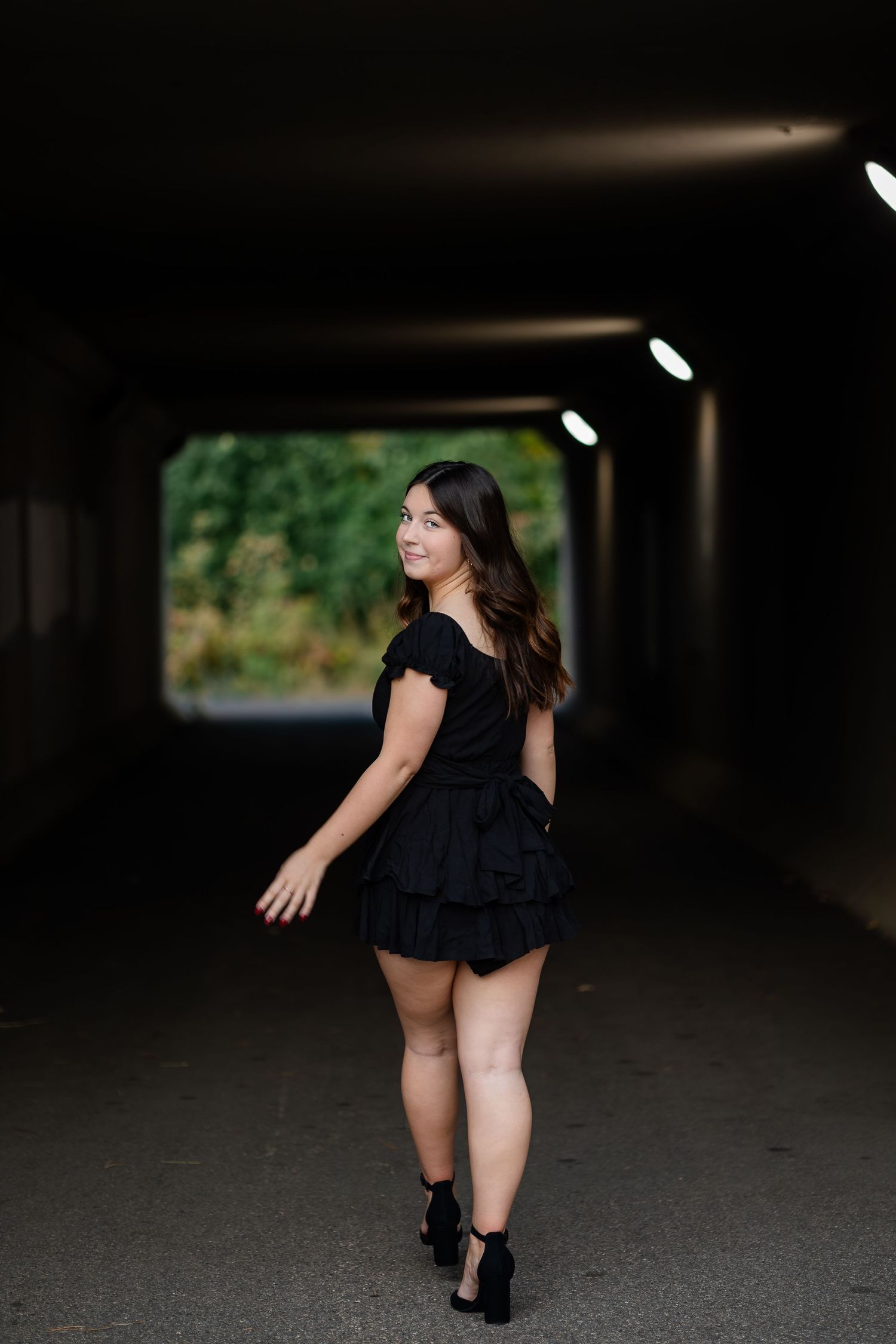 Figure in black dress poses in dark parking garage setting.