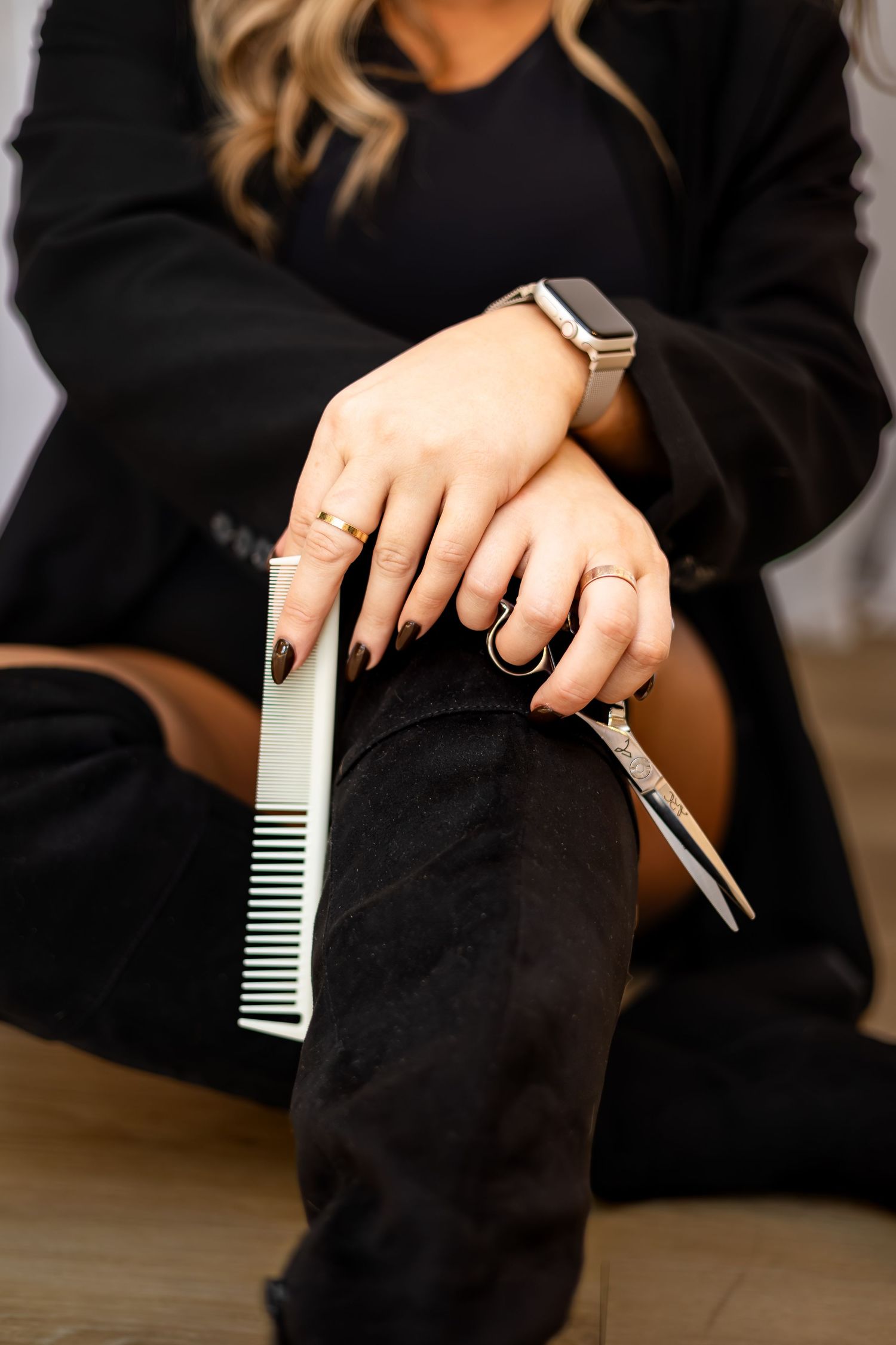 Close-up view of hands holding a wide-toothed comb against black fabric, showing detail of rings and manicured nails.