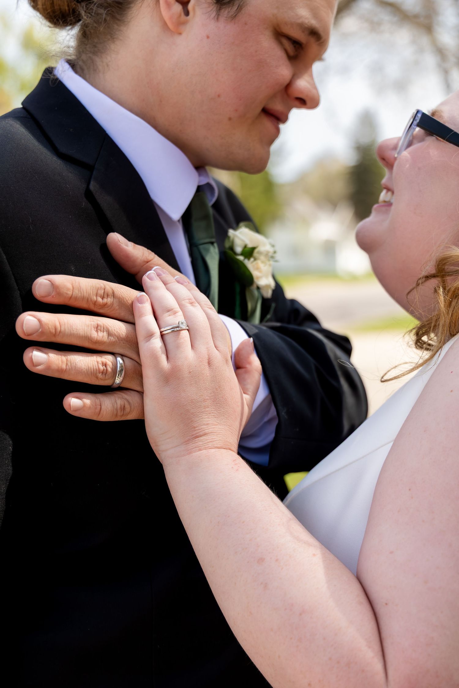 Close-up of newlyweds showing wedding rings while embracing outdoors after ceremony.