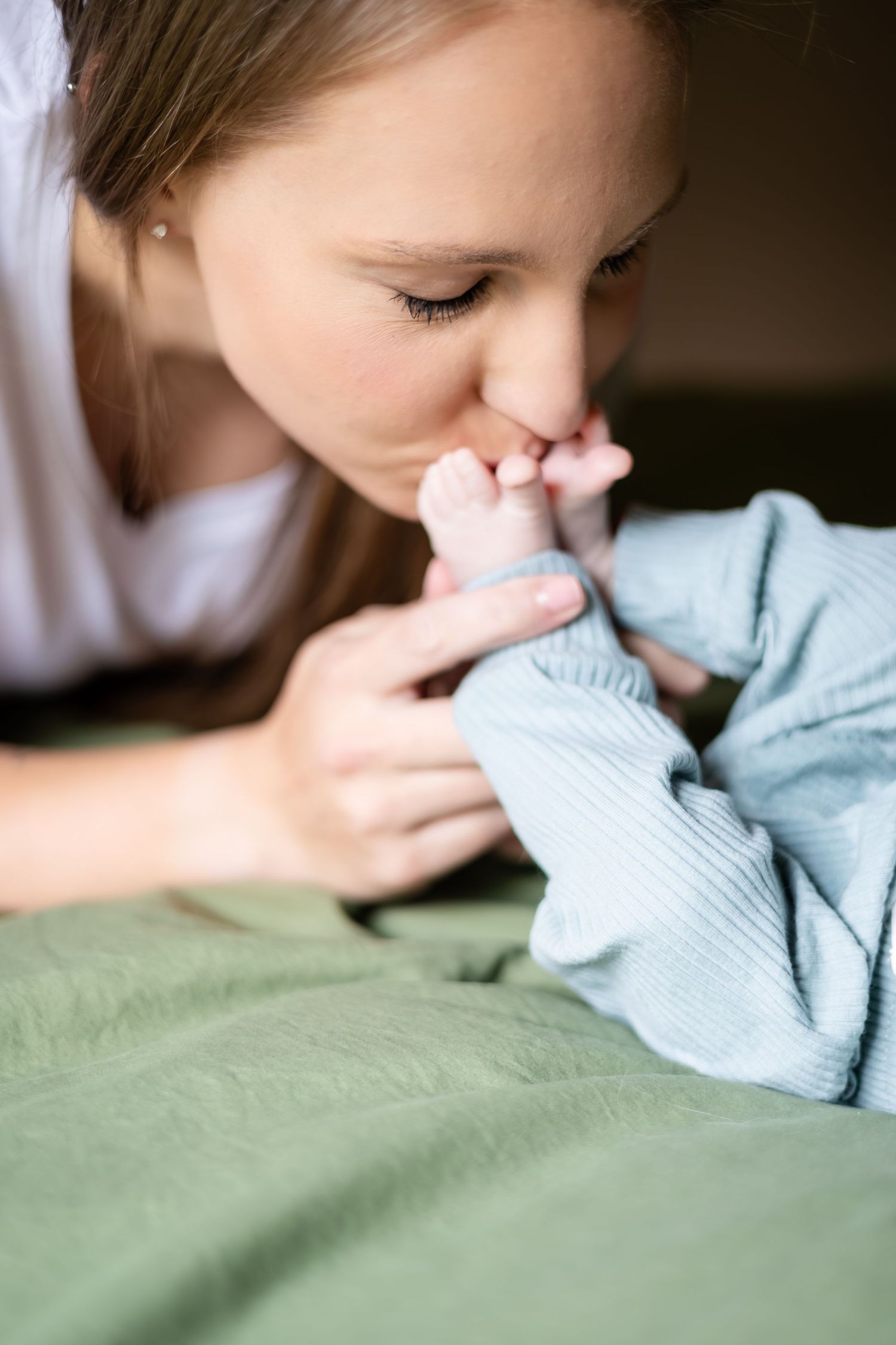 Tender moment of parent kissing baby's tiny feet on green bedding.
