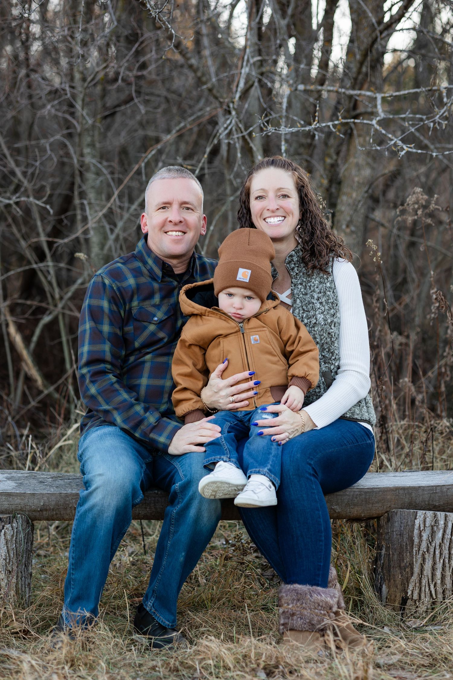 Family sitting together on a rustic wooden bench in a wooded outdoor setting during winter.