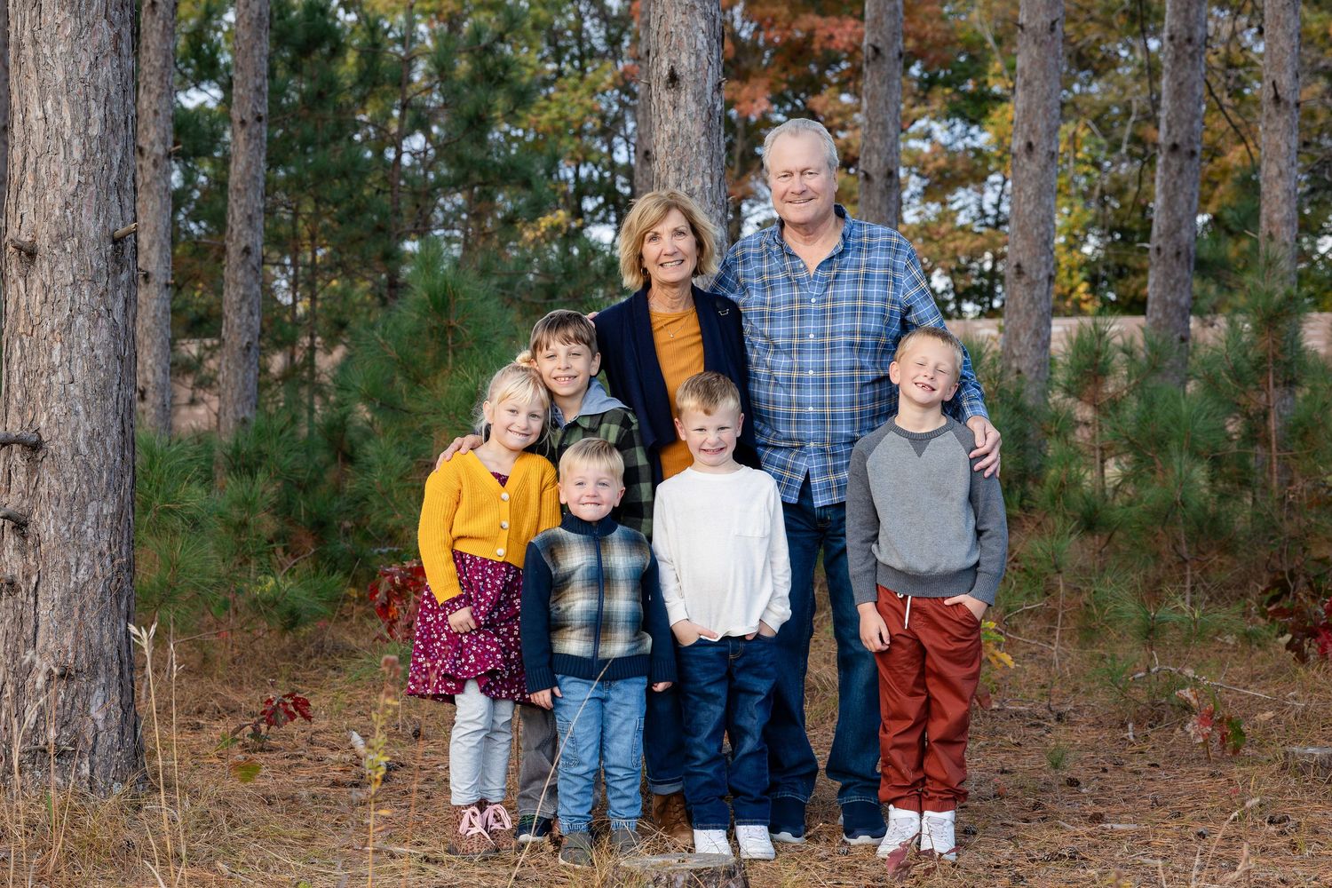 Extended family gathering for a group portrait in a wooded setting during fall.