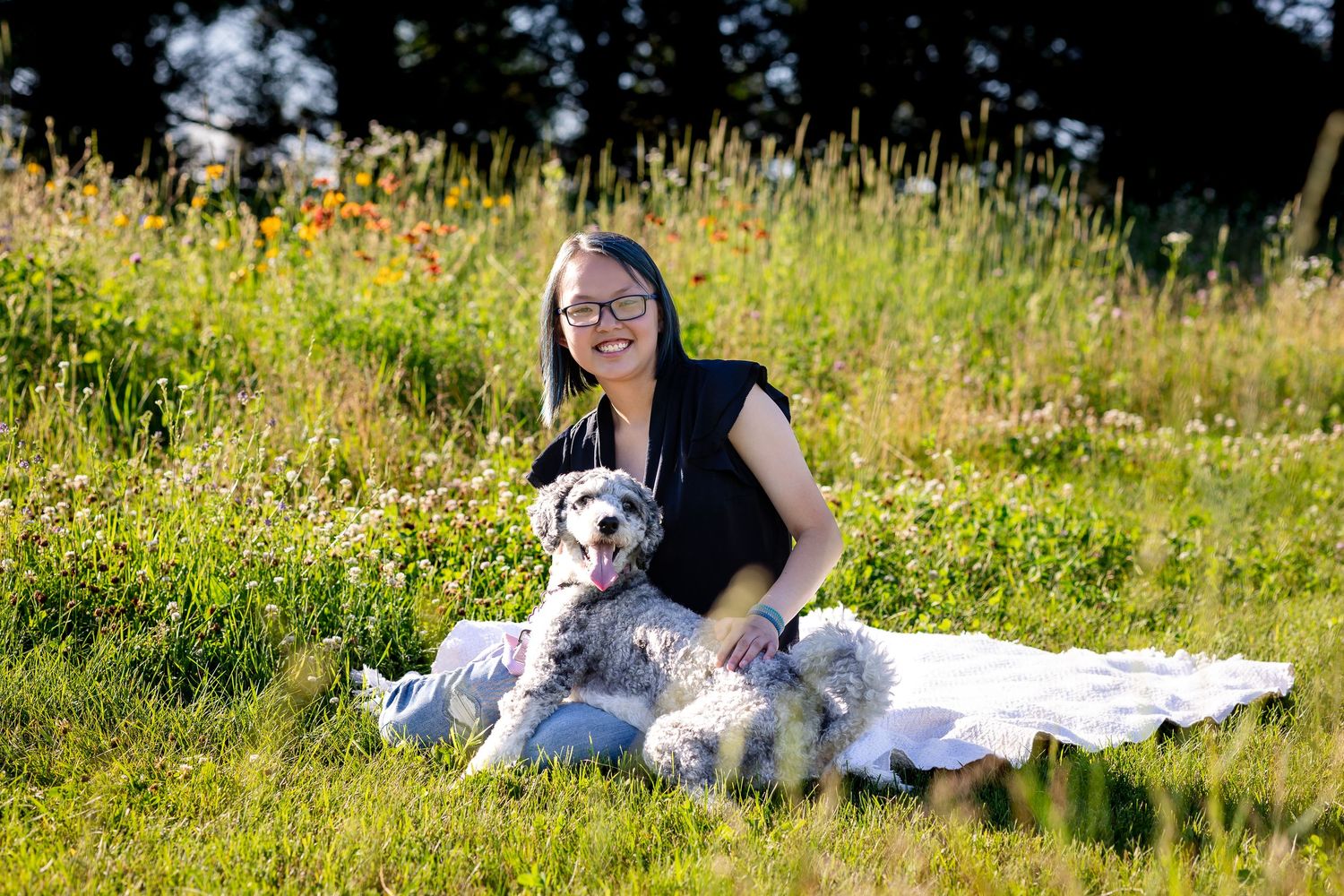 Graduate and dog relaxing together on blanket in summer meadow.