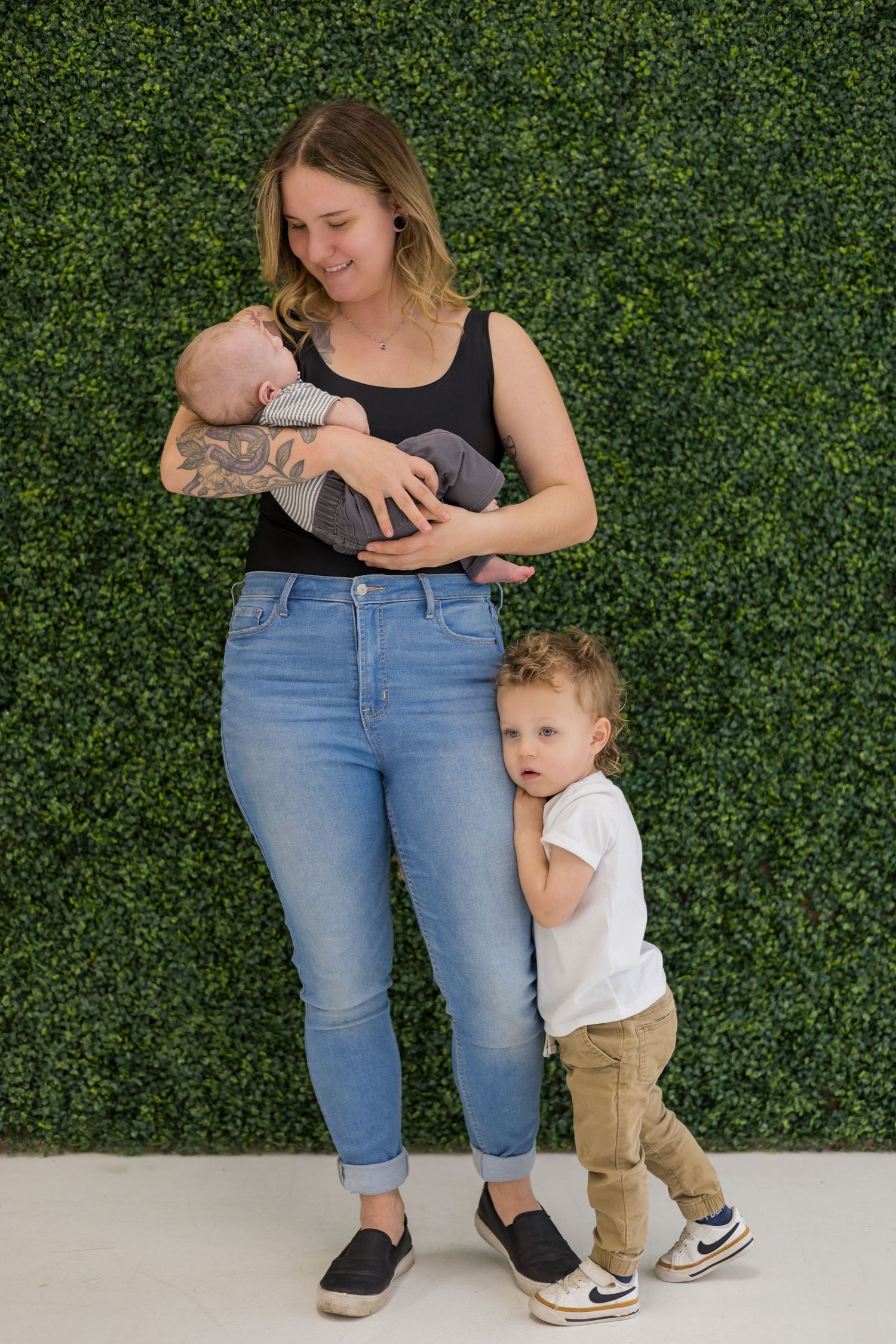 A casual family portrait against a green hedge with denim and casual attire.