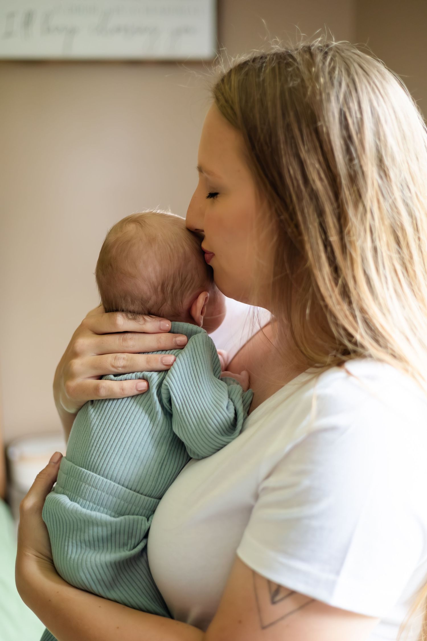 Parent in white t-shirt cradling infant wearing mint green outfit.