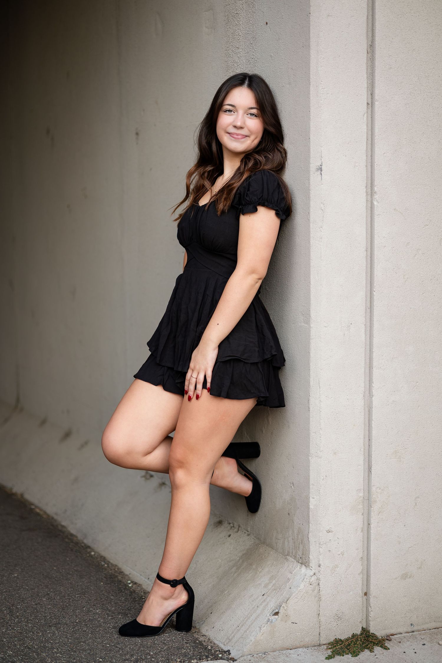 Model in black dress poses against concrete wall in artistic portrait series.