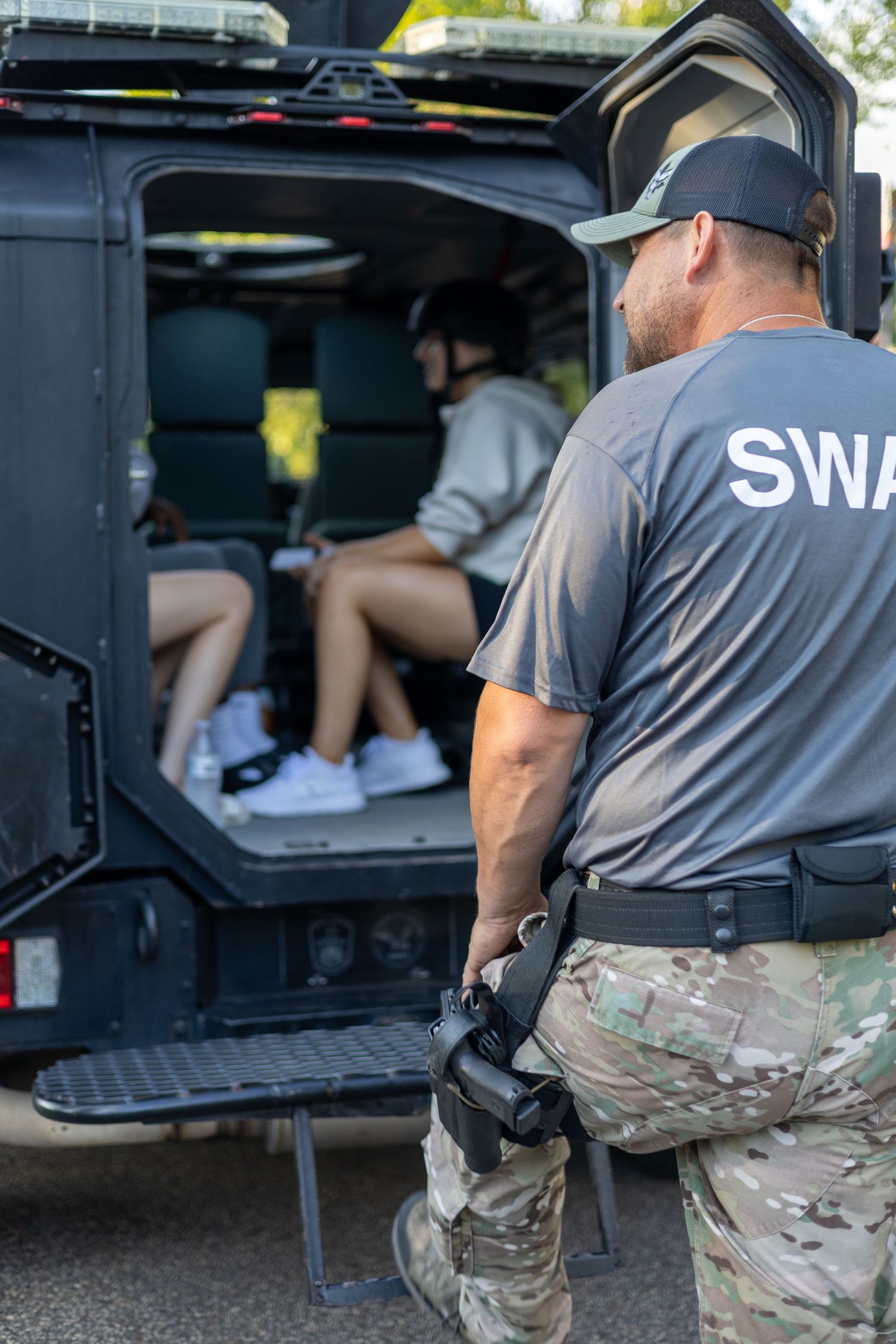 SWAT officers in tactical gear standing by open compartments of an armored vehicle.