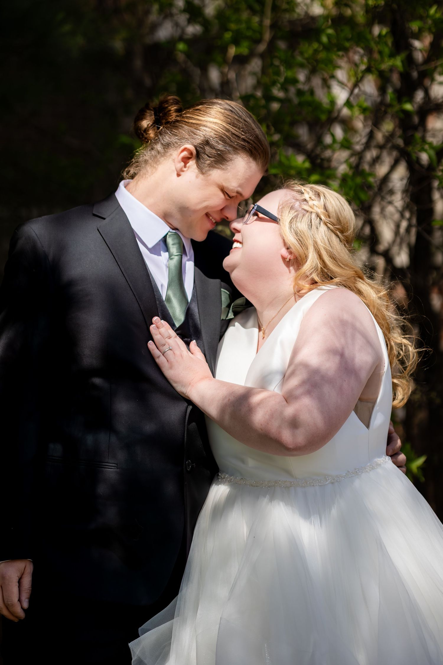 Bride and groom share an intimate moment, touching foreheads and smiling on their wedding day outdoors.