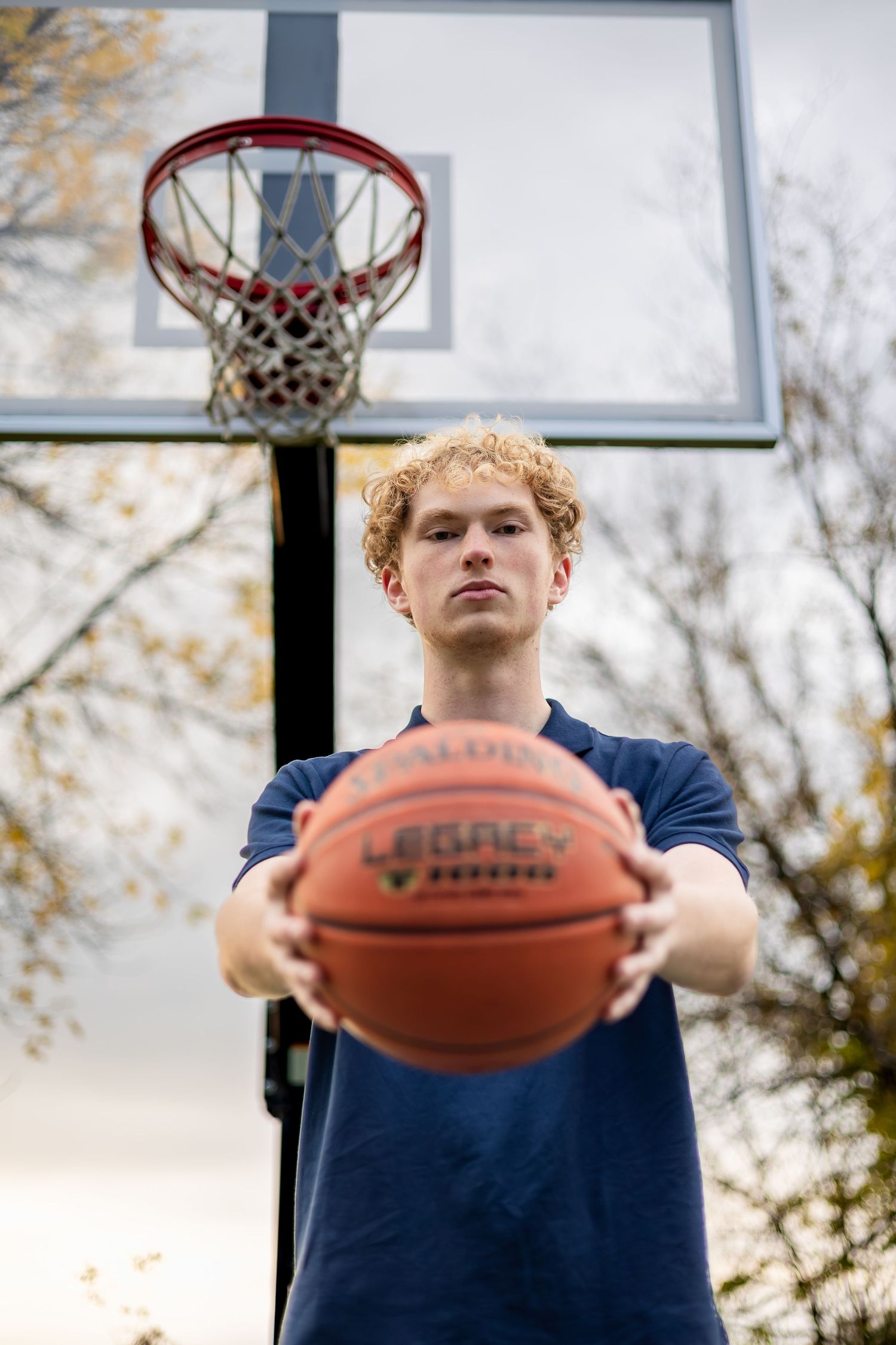 Basketball player in navy shirt holds ball in front of outdoor hoop during practice session.