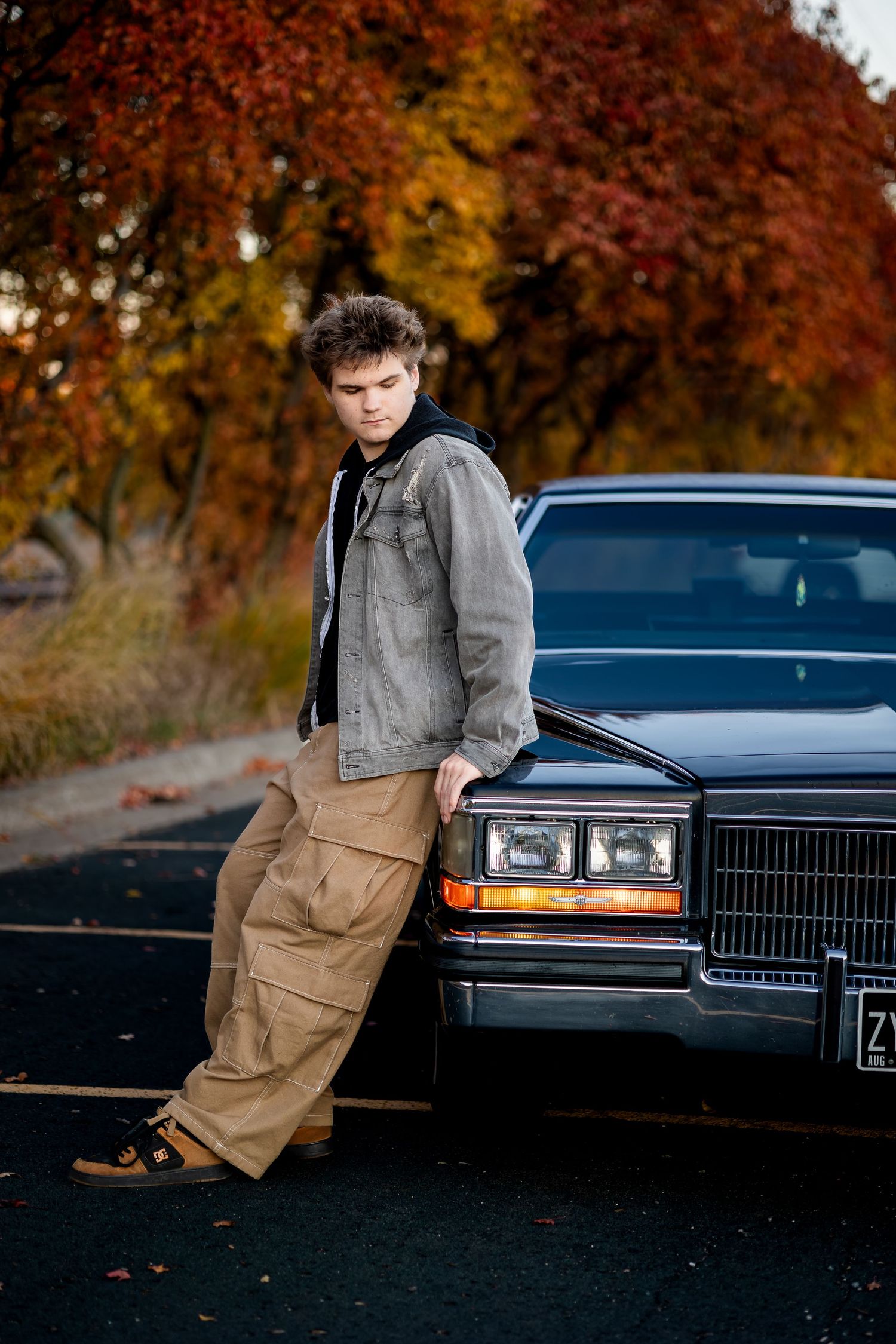 A classic black Cadillac car photographed during fall season with autumn foliage in the background.