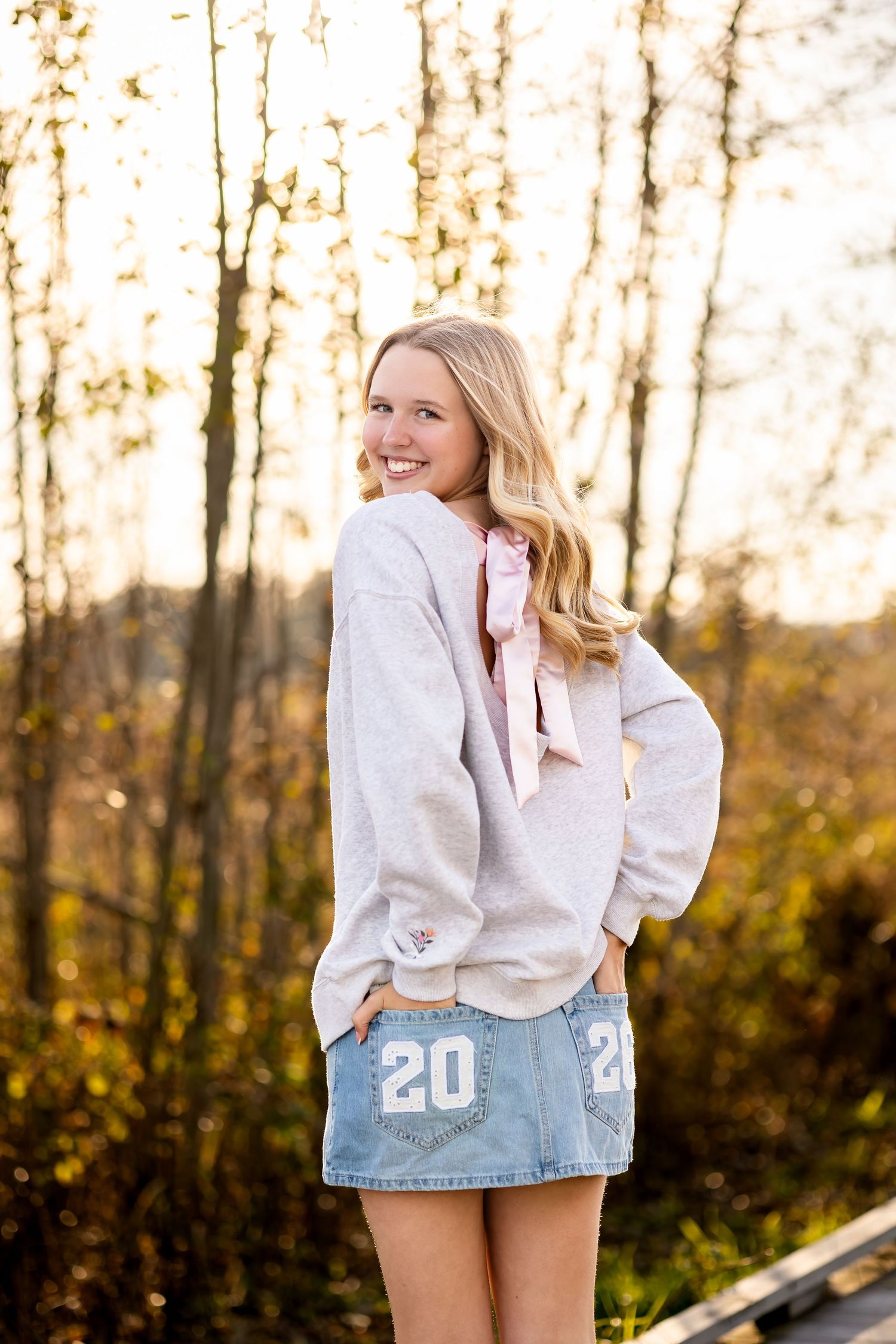 Athletic casual portraits in denim shorts and white sweater against autumn trees at golden hour.