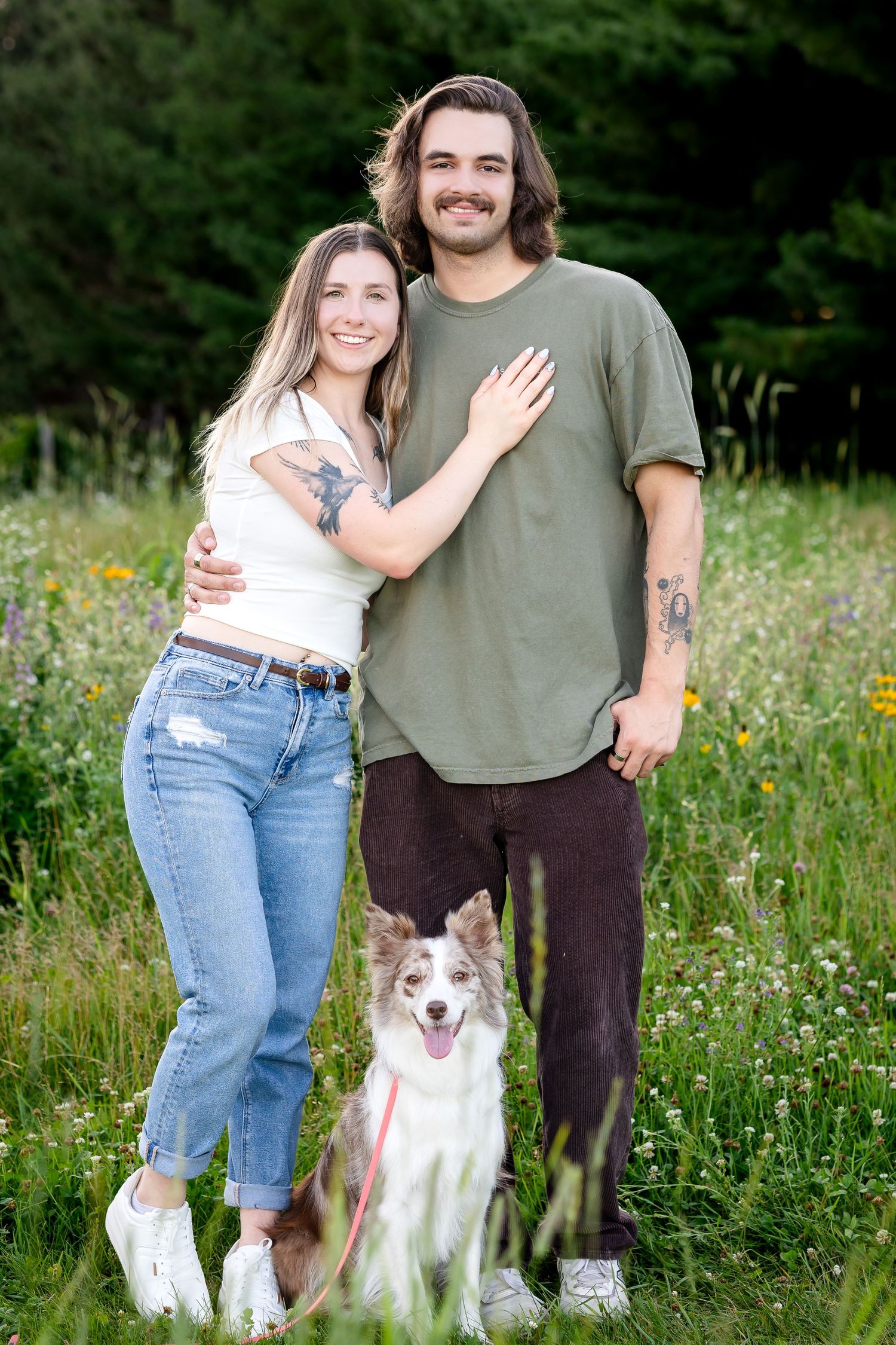 Casual couple with their happy border collie dog in a wildflower meadow.