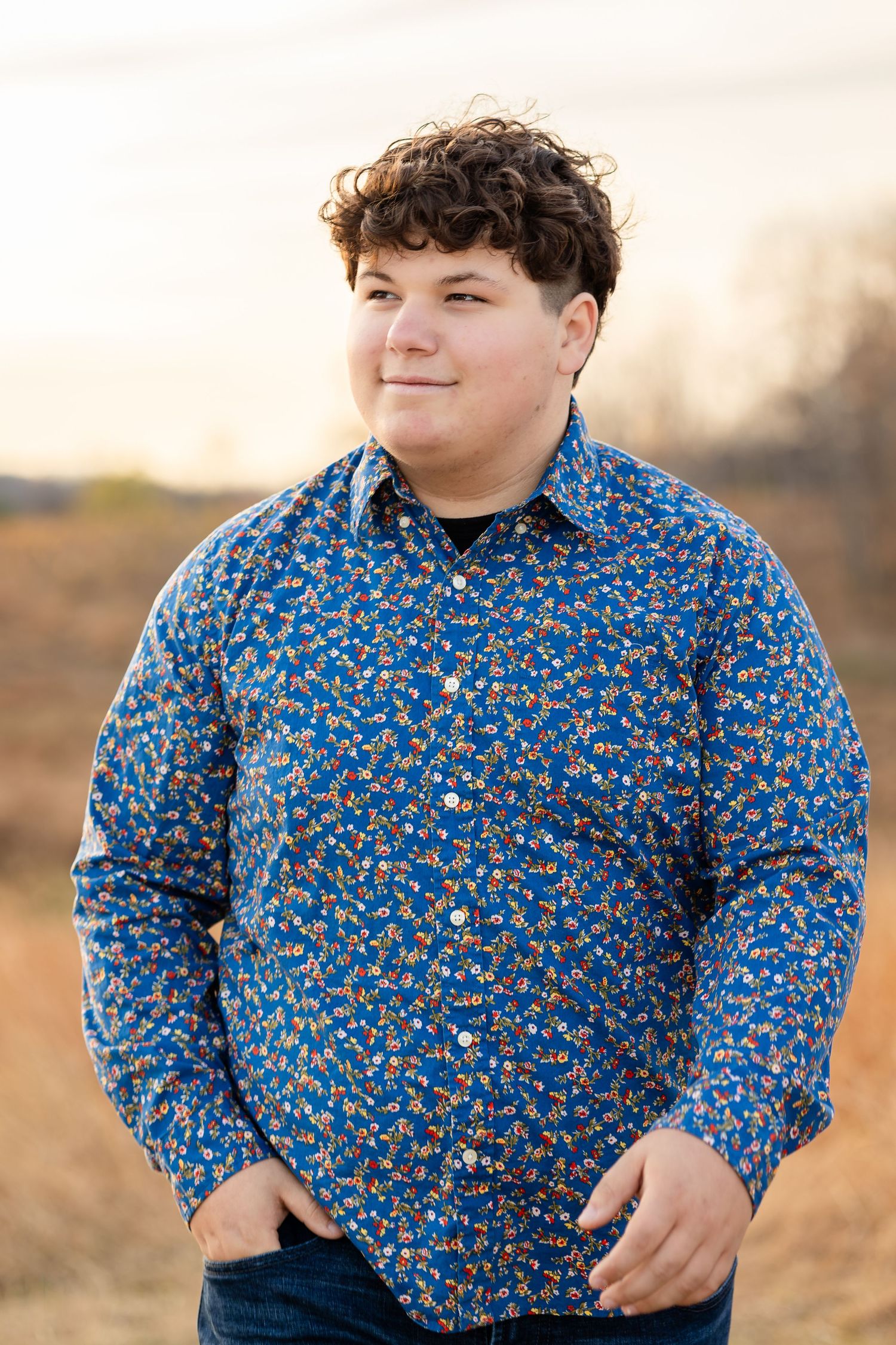 Person wearing a vibrant blue floral shirt poses against a warm outdoor background.
