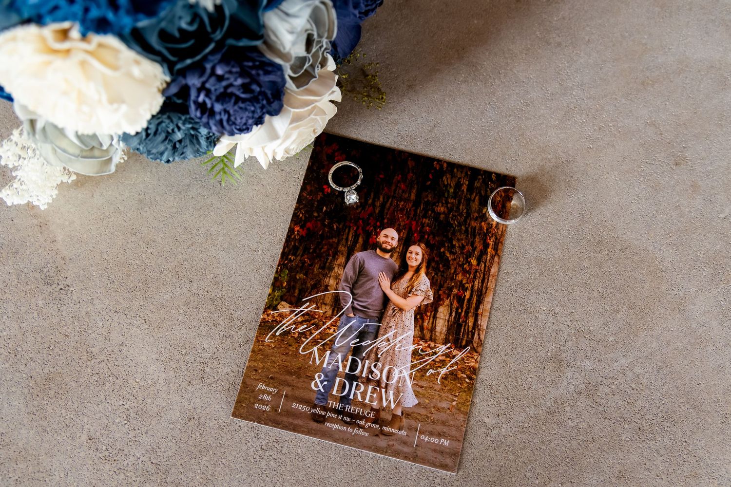 Wedding invitation featuring couple's photo with names Madison and Drew beside blue floral bouquet.