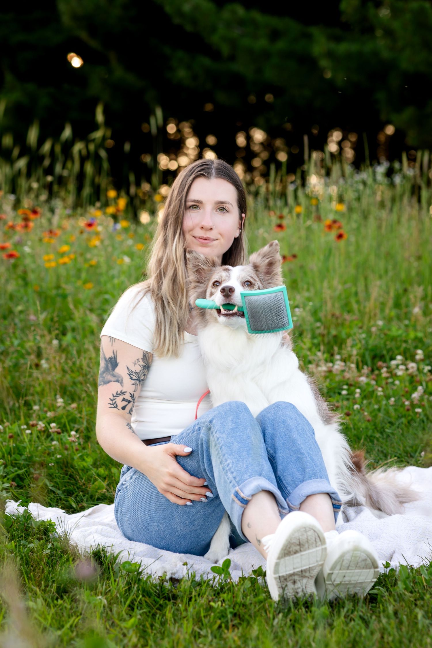 Person relaxing on blanket in wildflower meadow with white fluffy dog on sunny summer day.