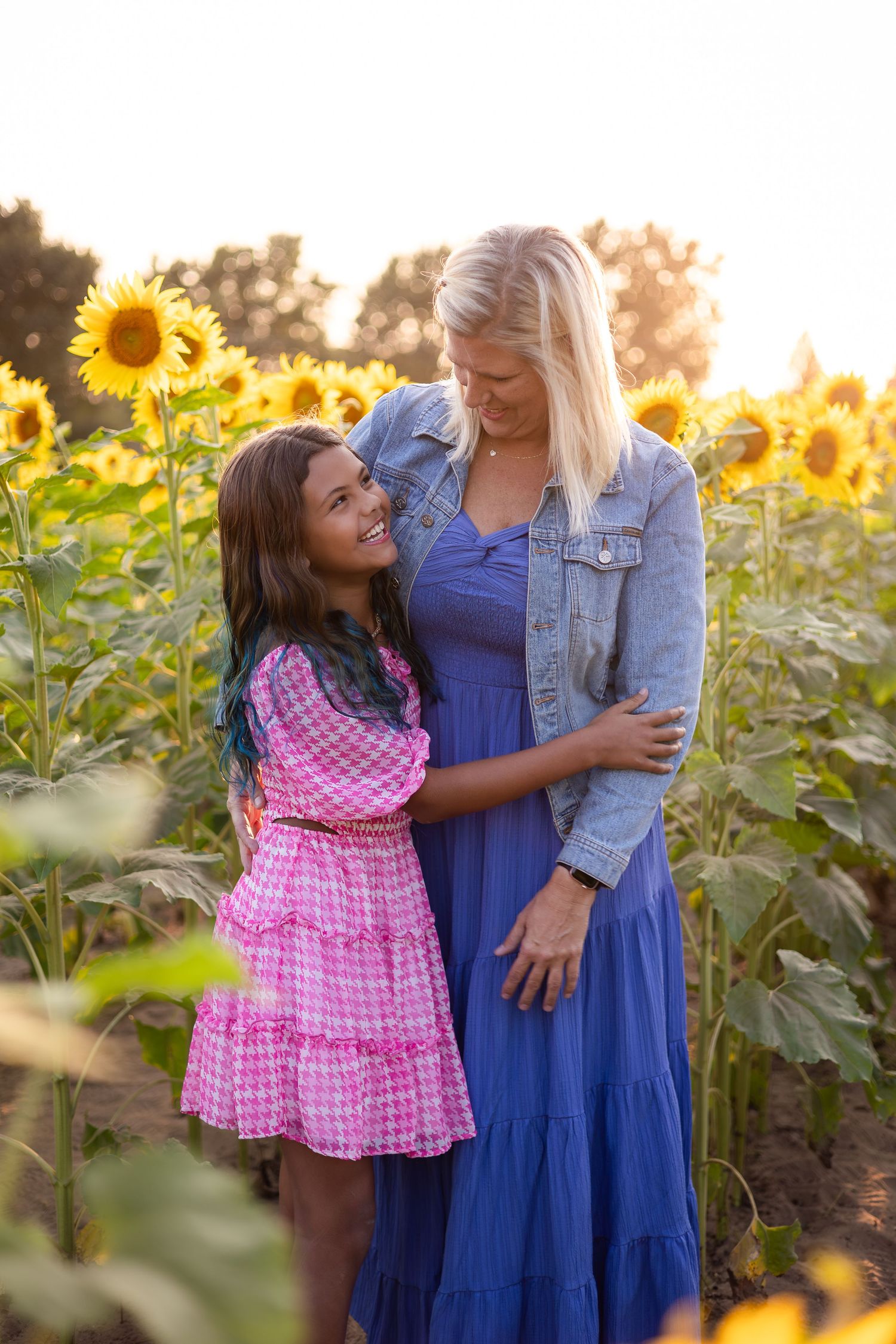 Two people share a tender moment among blooming sunflowers at golden hour.