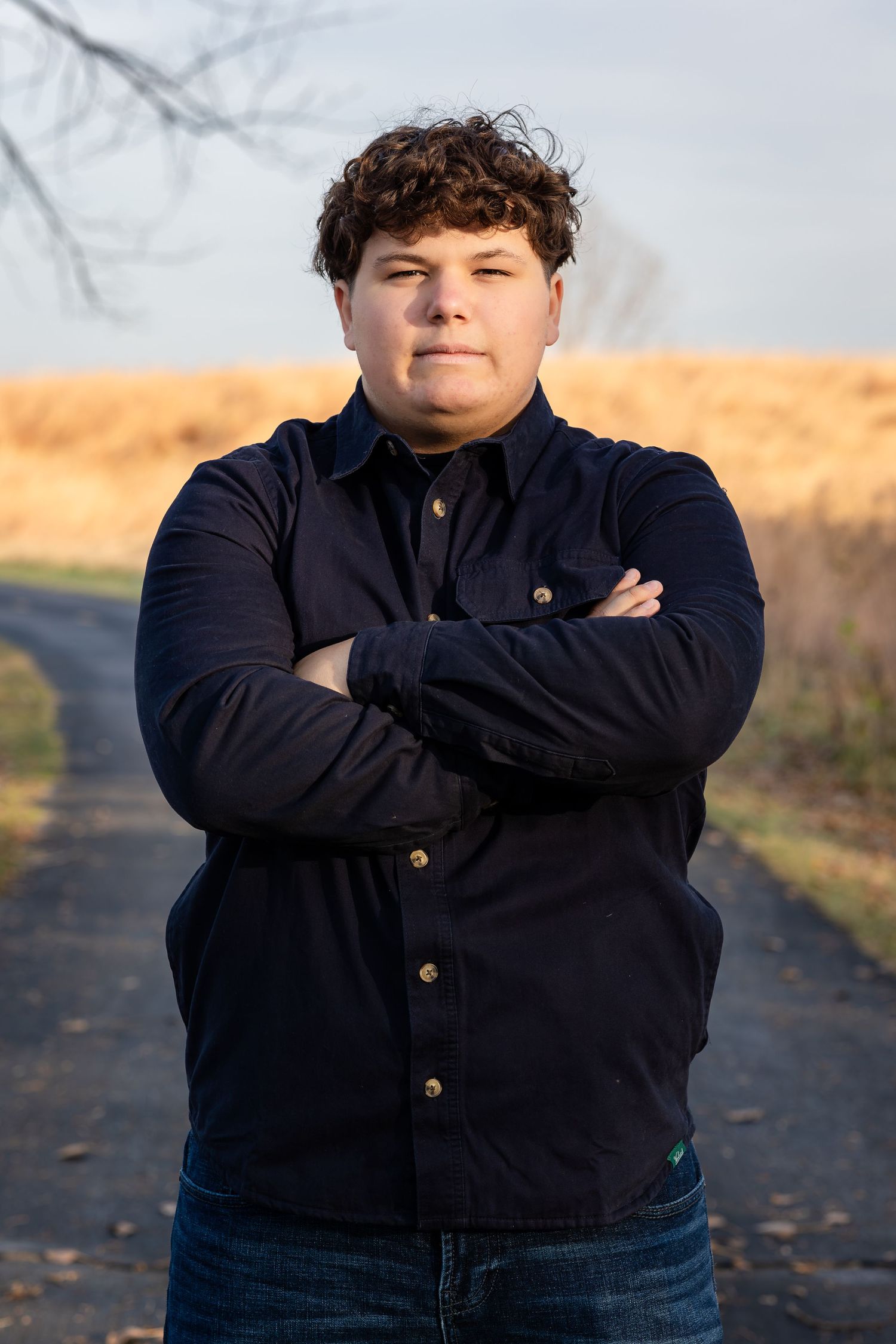 Portrait of someone wearing a navy button-up shirt against an autumn outdoor background.
