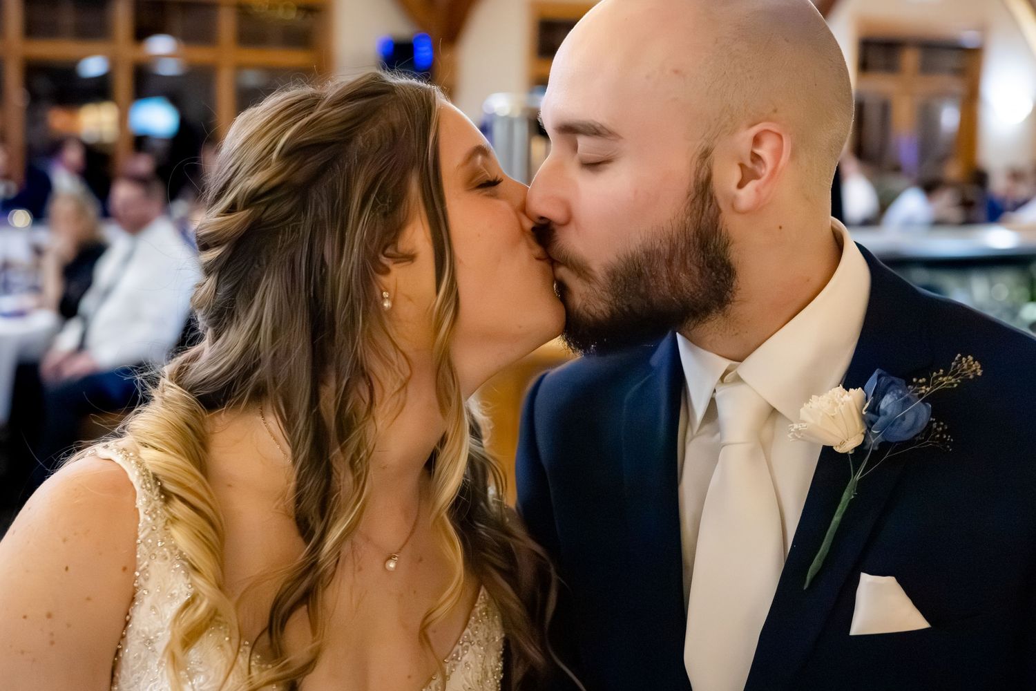 Bride and groom sharing first kiss in navy suit with white rose boutonniere.