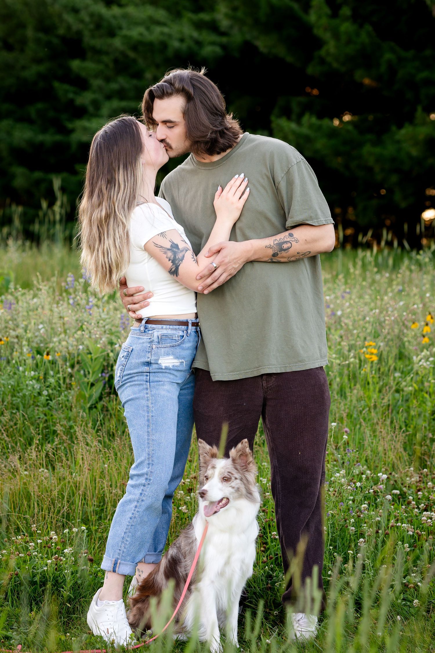 Couple sharing romantic moments with their dog in a wildflower field at sunset.