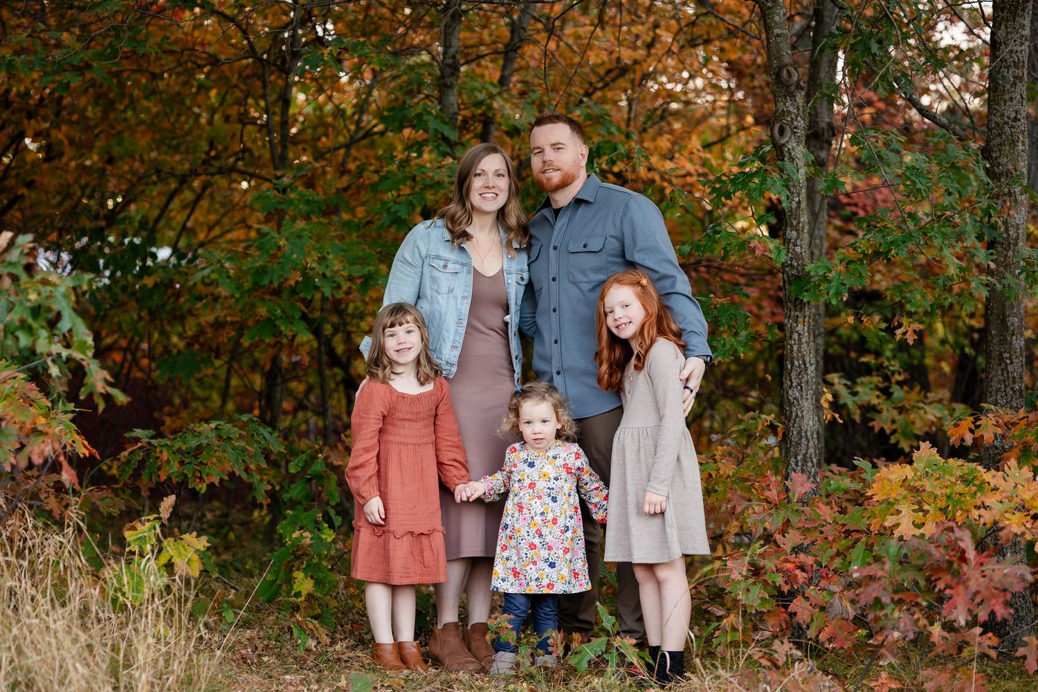 Family portrait session in autumn woods with coordinated outfits in rust, gray and denim tones.