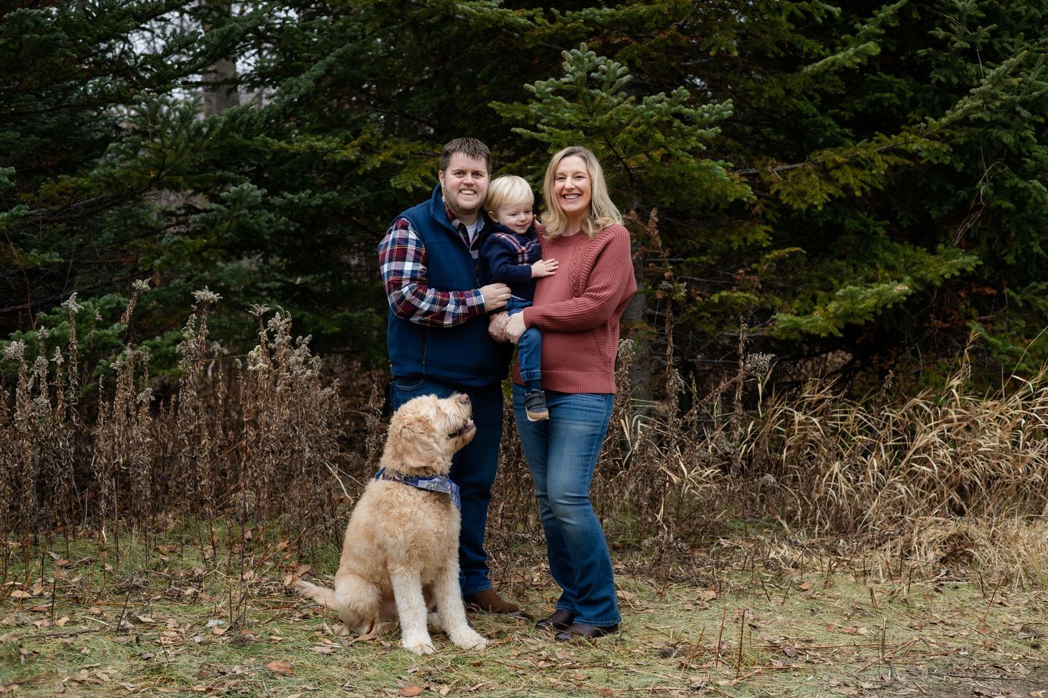 A group poses outdoors against a backdrop of evergreen trees and natural brush.