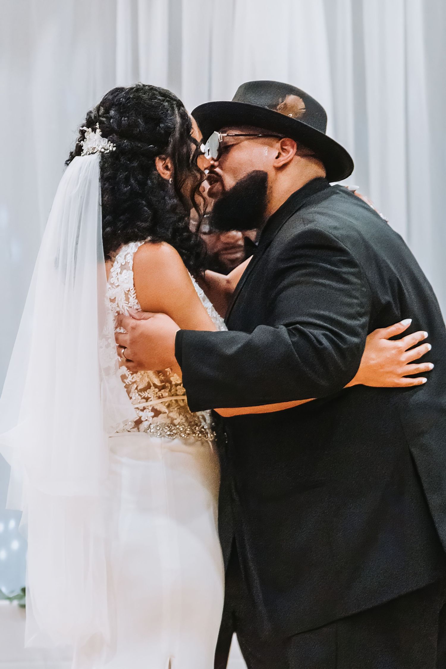 Wedding couple embracing against white backdrop in formal attire.
