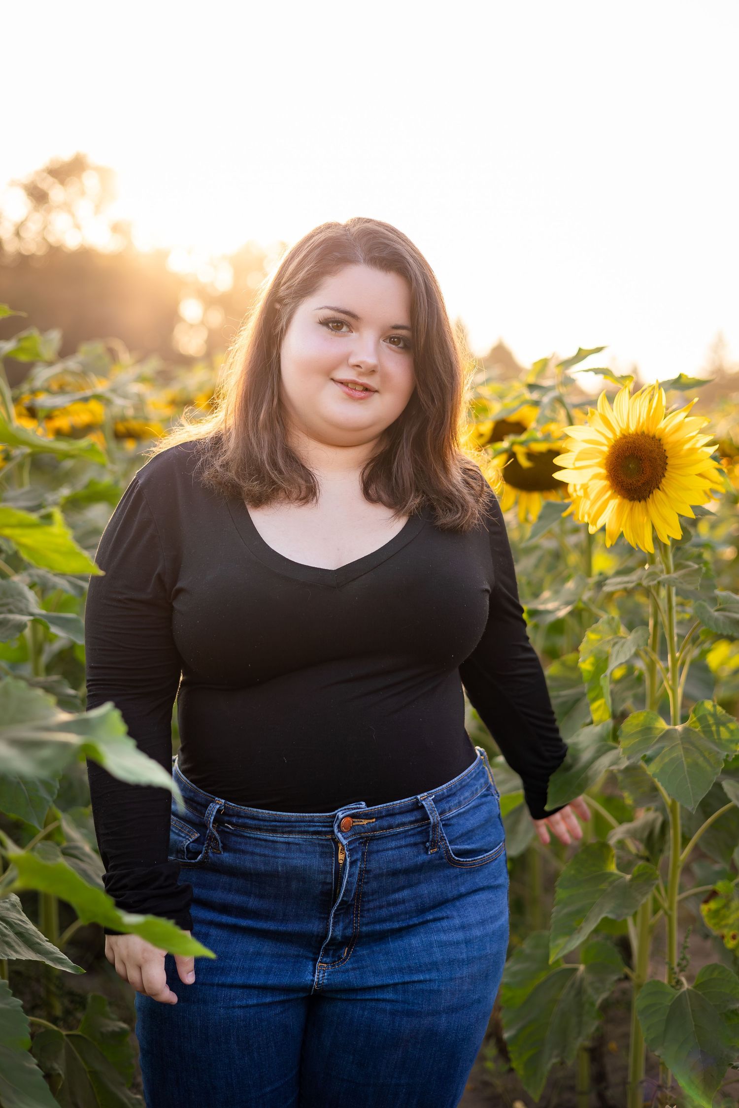 Woman in black top poses confidently in sunflower field at golden hour.